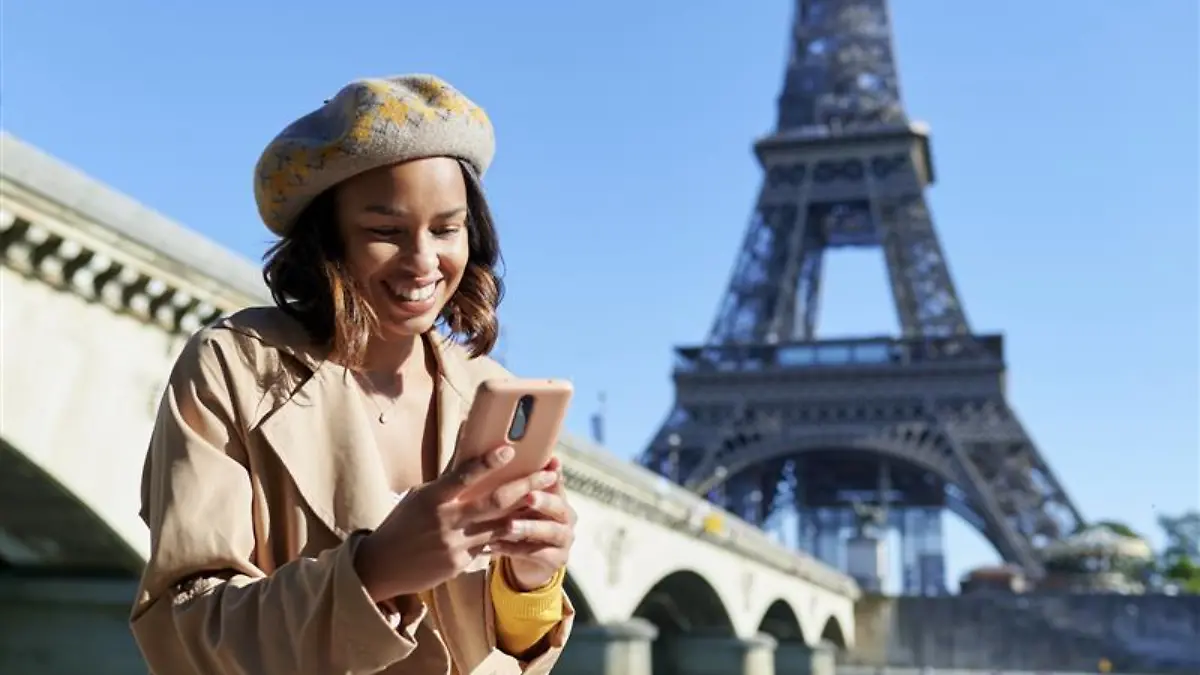 Frau trägt beigen Mantel vor Eiffelturm und Seine.