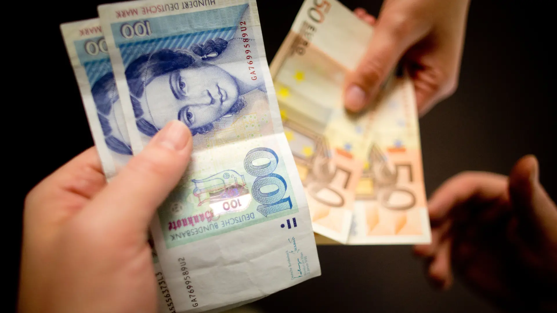 Zwei Hände tauschen Scheine miteinander aus. Die Hand gibt alte D-Mark, die andere neue Euro.