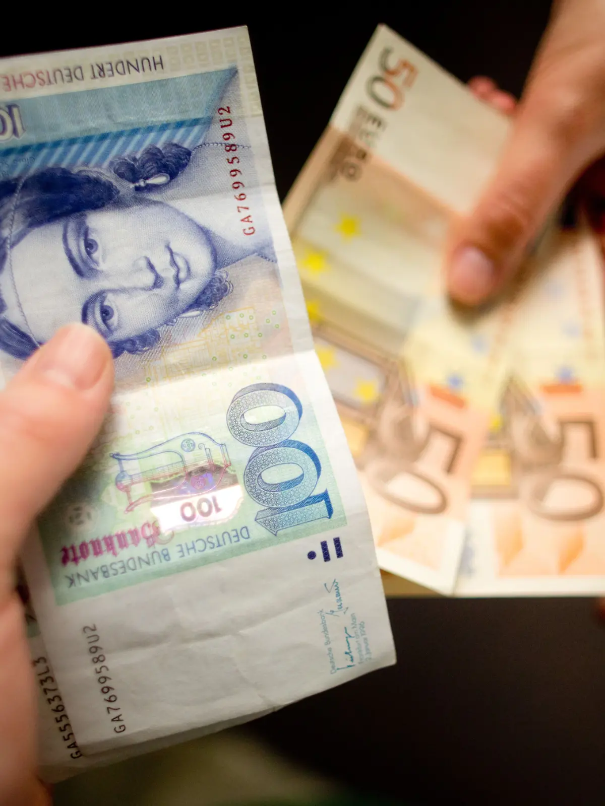 Zwei Hände tauschen Scheine miteinander aus. Die Hand gibt alte D-Mark, die andere neue Euro.