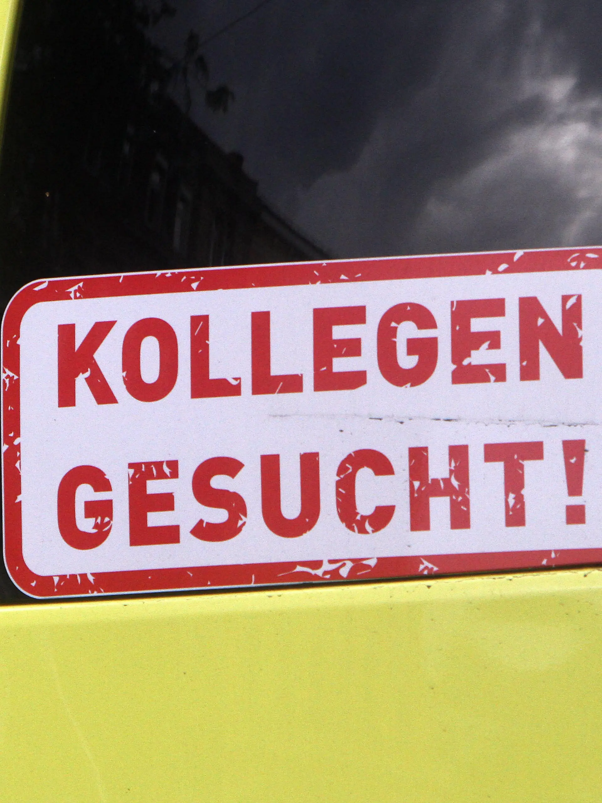  Aufkleber mit Aufschrift Kollegen gesucht klebt am Rückfenster eines Krankentransportwagen s in der Innenstadt von Heidelberg, Baden Württemberg, Deutschland *** Sticker with the inscription Colleagues wanted is stuck on the back window of an ambulance in downtown Heidelberg, Baden Württemberg, Germany