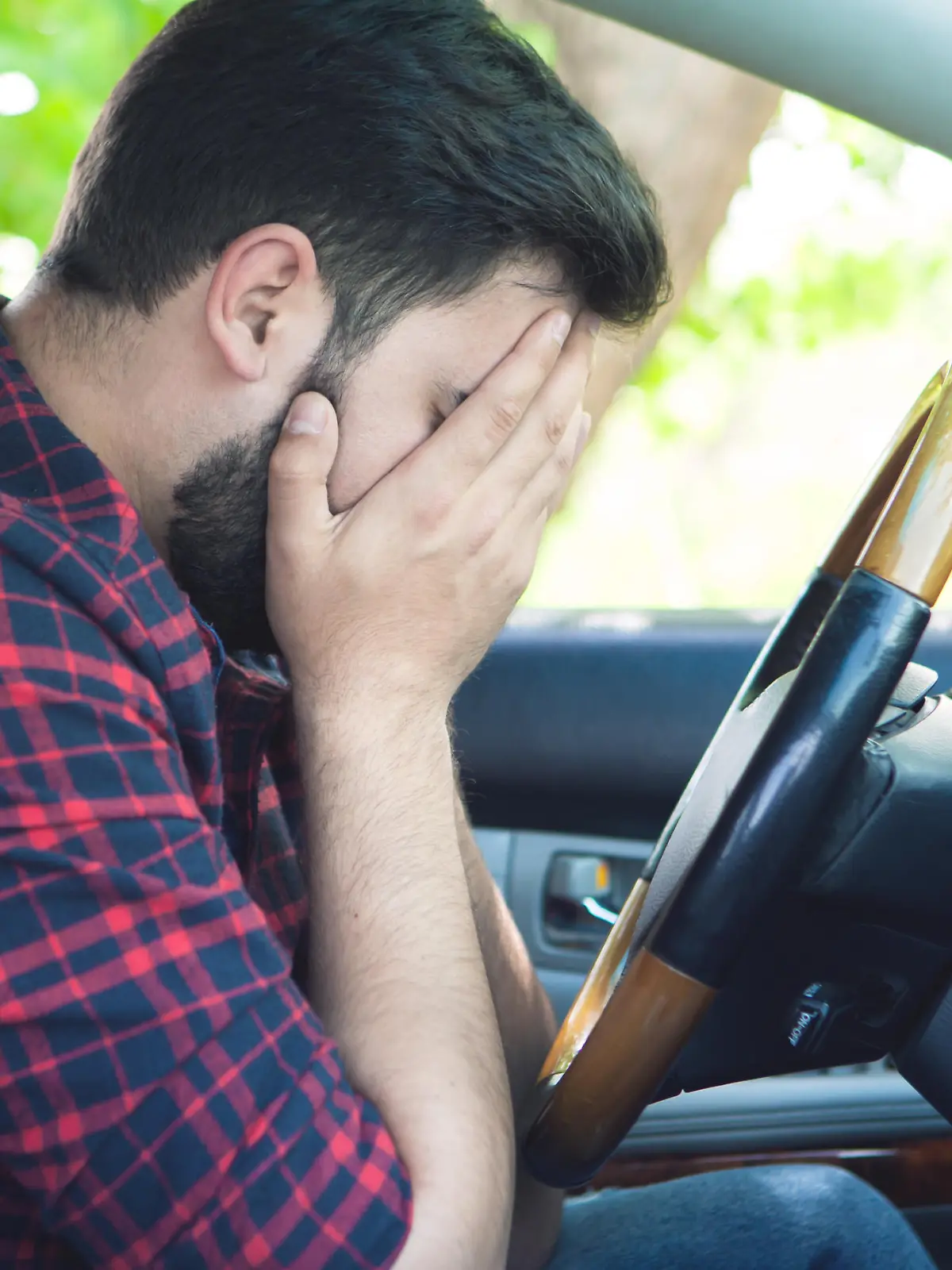 Ein junger Mann sitzt verzweifelt am Steuer seines Autos. Er hat das Gesicht in seinen Händen vergraben.