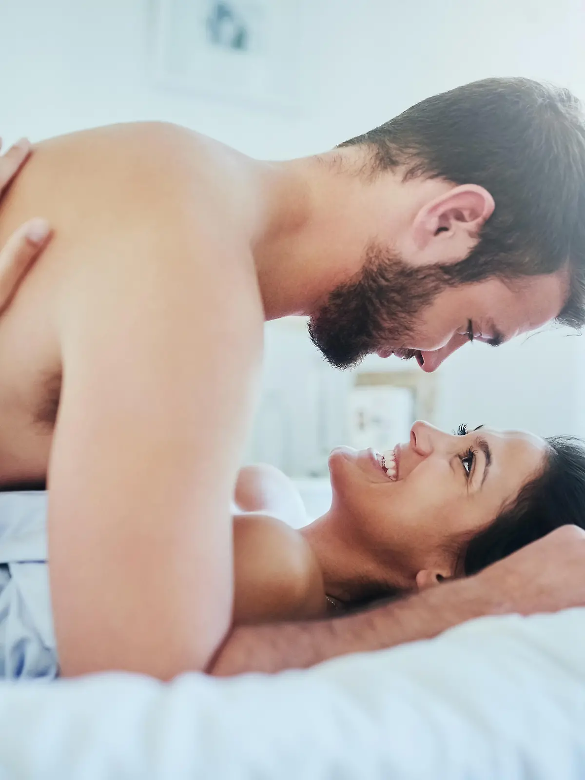 Ein junges Paar liegt gemeinsam im Bett und turtelt.