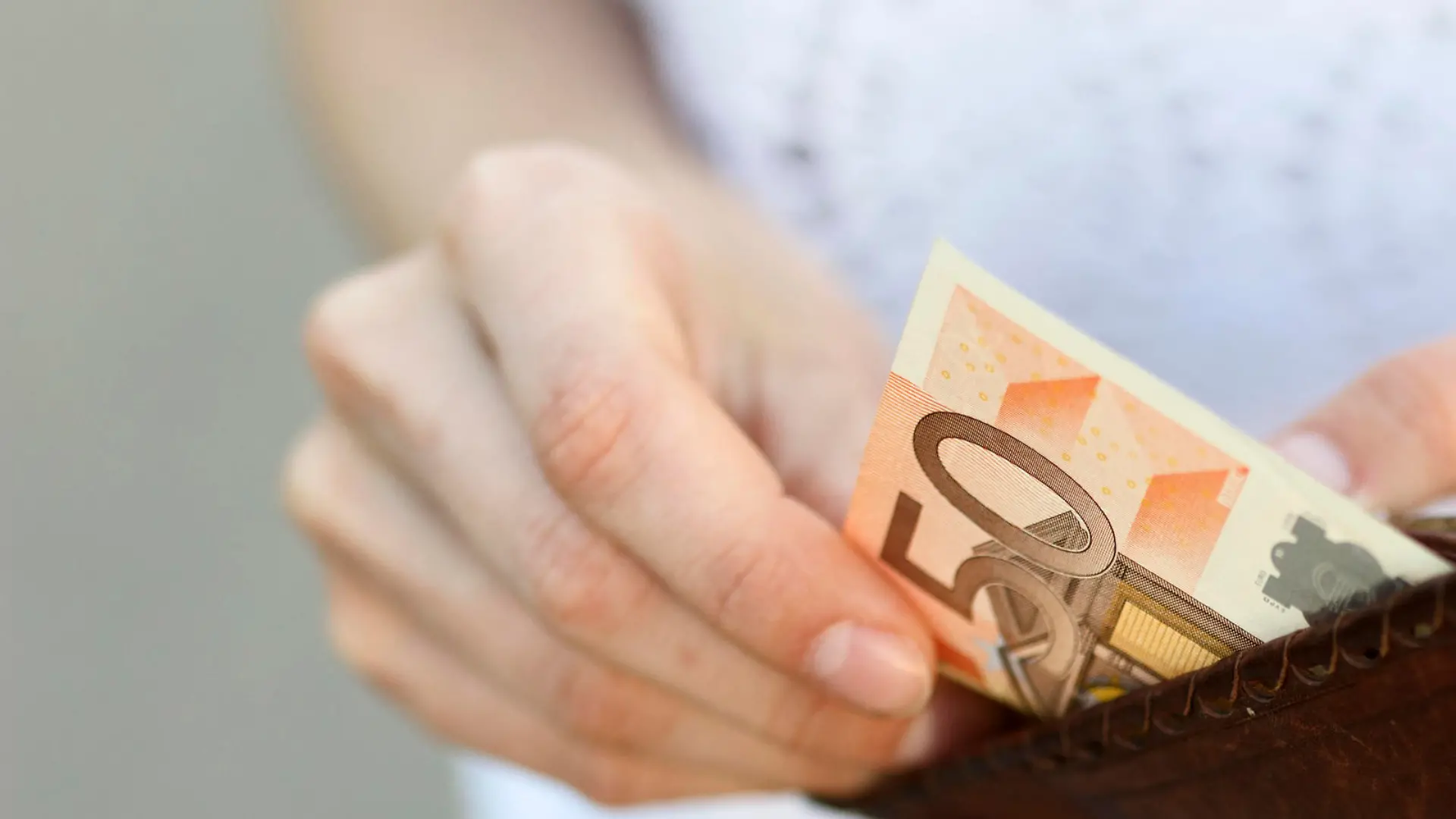 Girl is taking out a banknote of fifty euros from brown leather wallet on the street. Hands, money and wallet close-up