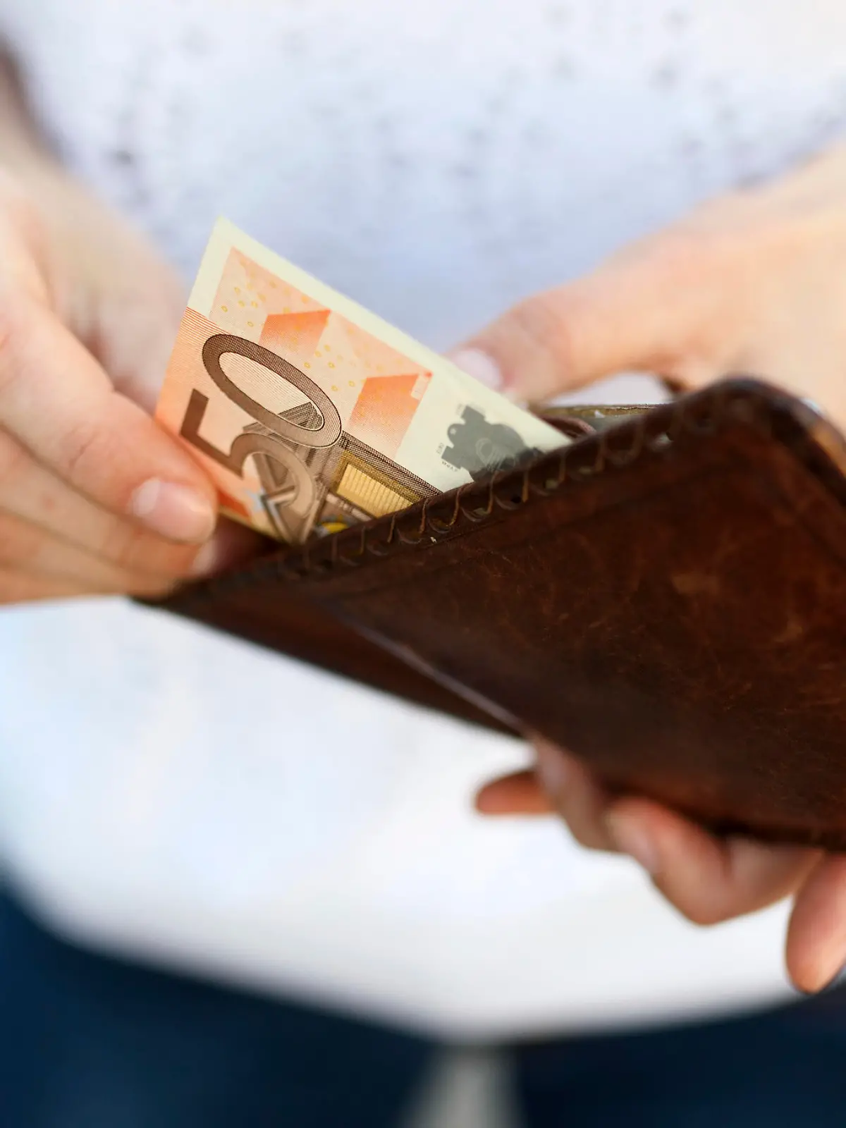 Girl is taking out a banknote of fifty euros from brown leather wallet on the street. Hands, money and wallet close-up
