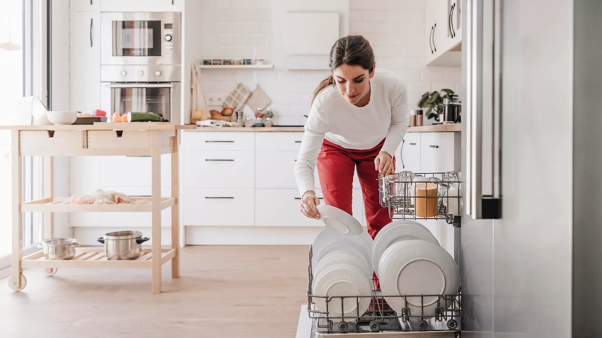 Woman arranging plates in dishwasher at home || Modellfreigabe vorhanden