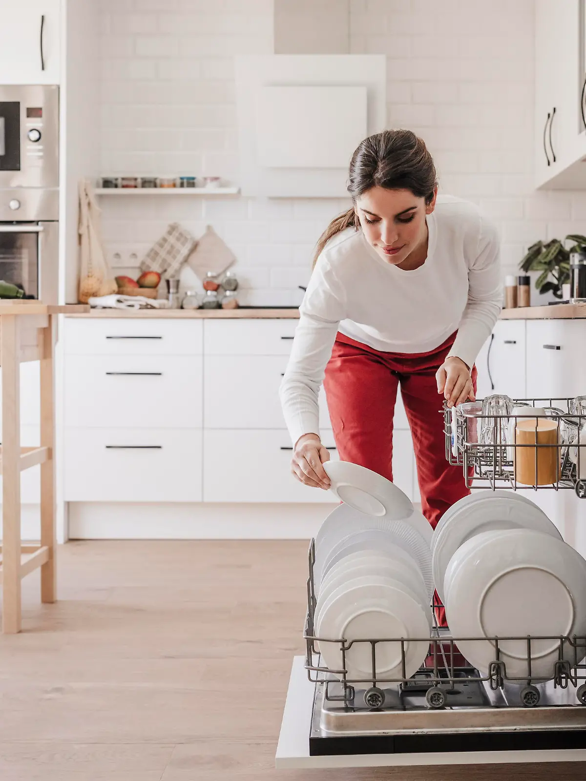 Woman arranging plates in dishwasher at home || Modellfreigabe vorhanden
