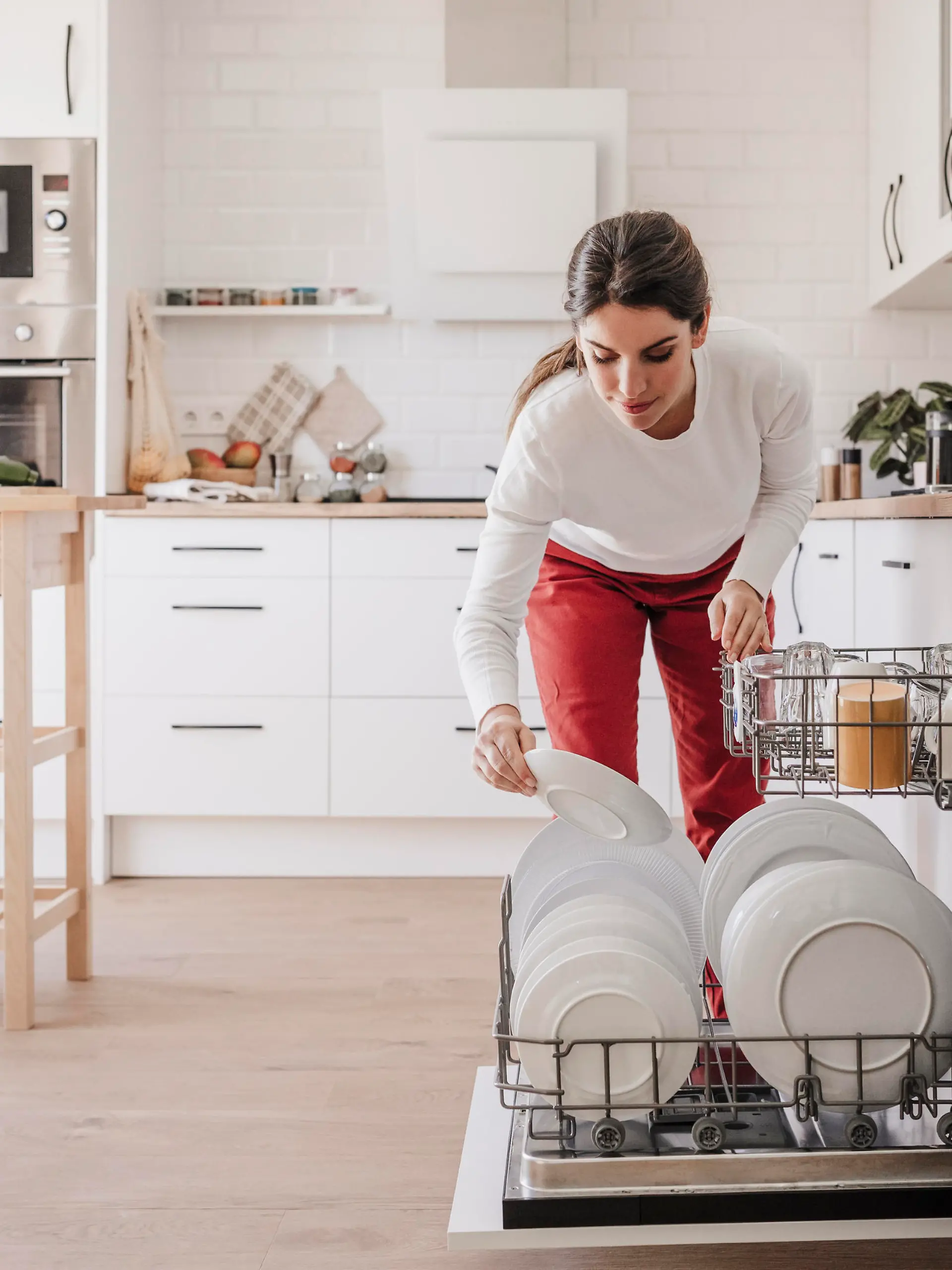 Woman arranging plates in dishwasher at home || Modellfreigabe vorhanden