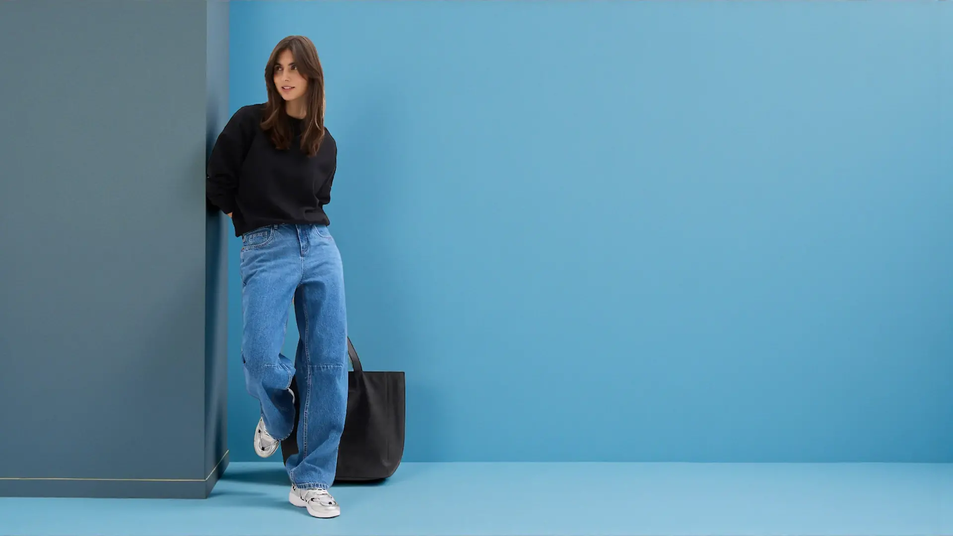 Frau trägt Barrel-Jeans vor blauem Hintergrund.
