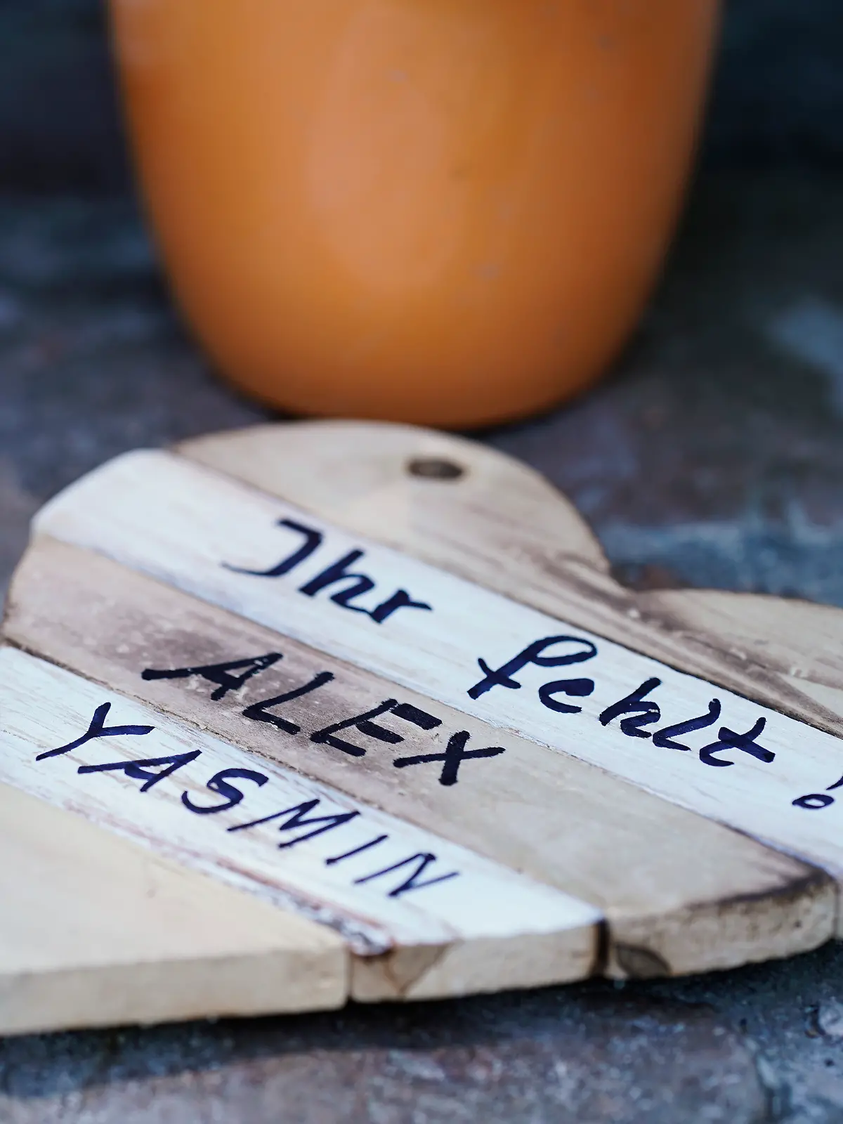 Auf einem Holzbrett in Herzform ist an einer Landstraße zwischen Kusel und Ulmet an einer Gedenkstätte für zwei getötete Polizisten die Aufschrift „Ihr fehlt! Alex Yasmin“ aufgebracht.