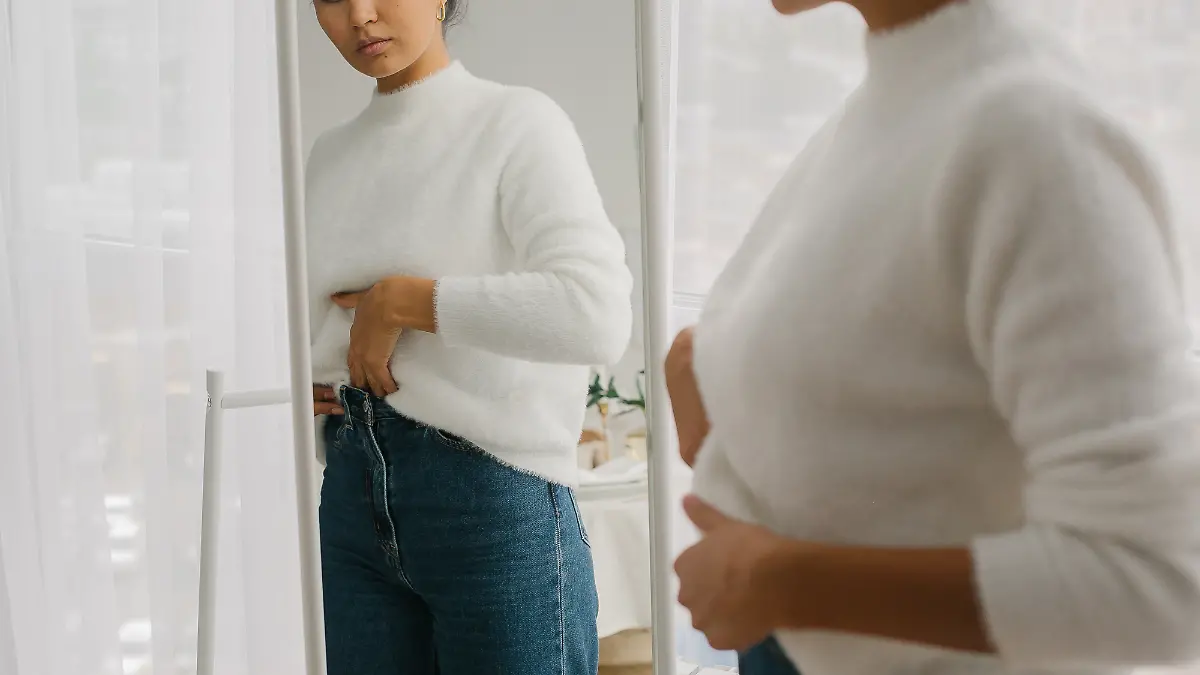 Frau in Jeans und Strickpullover vor dem Spiegel.