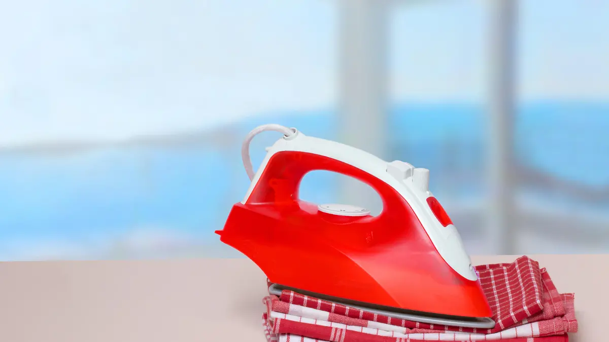 Closeup of a red iron on a stack red and white checkered towels on table against an abstract bright backgound. Advertising for the laundry service with space for design.