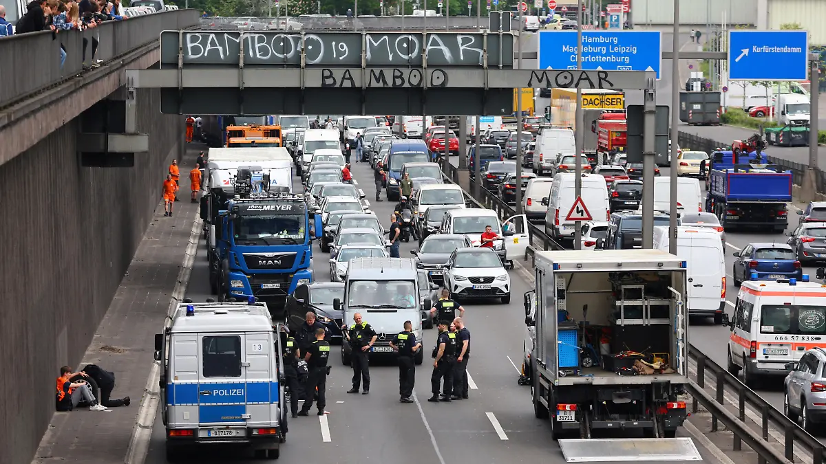 A general view shows the scene, as a police man removes glue from a hand of an activist of the "Letzte Generation" (Last Generation), who previously glued himself to a tire of a car while blocking the central highway A100, to protest for climate councils, a speed limit on highways as well as for affordable public transport, in Berlin, Germany May 15, 2023. REUTERS/Fabrizio Bensch
