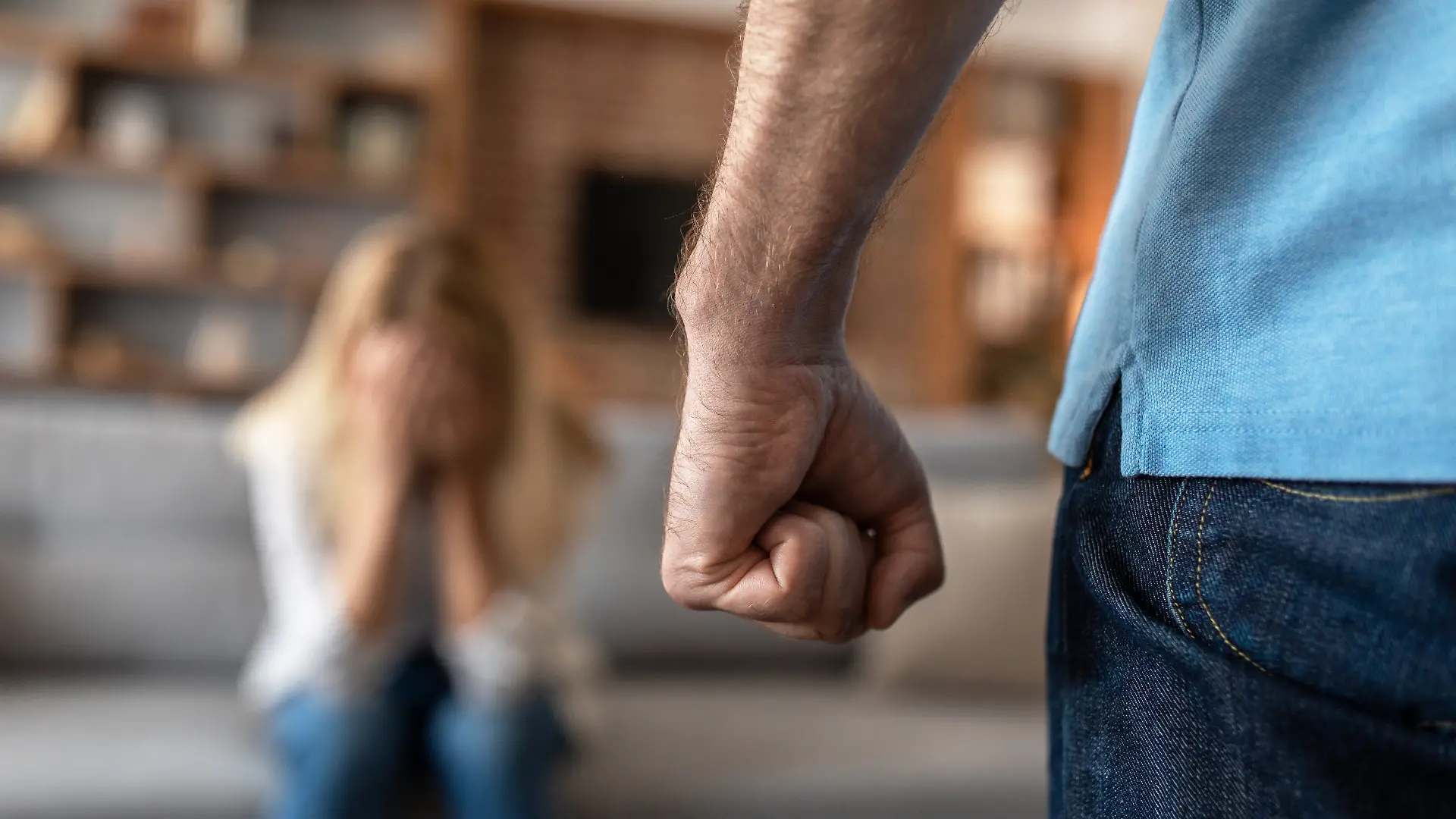 Eine verängstigte, weinende Frau fürchtet ihren Mann, der sie im Wohnzimmer mit der Faust bedroht (Nahaufnahme). Beziehungsprobleme, Missbrauch, Schläge und häusliche Gewalt