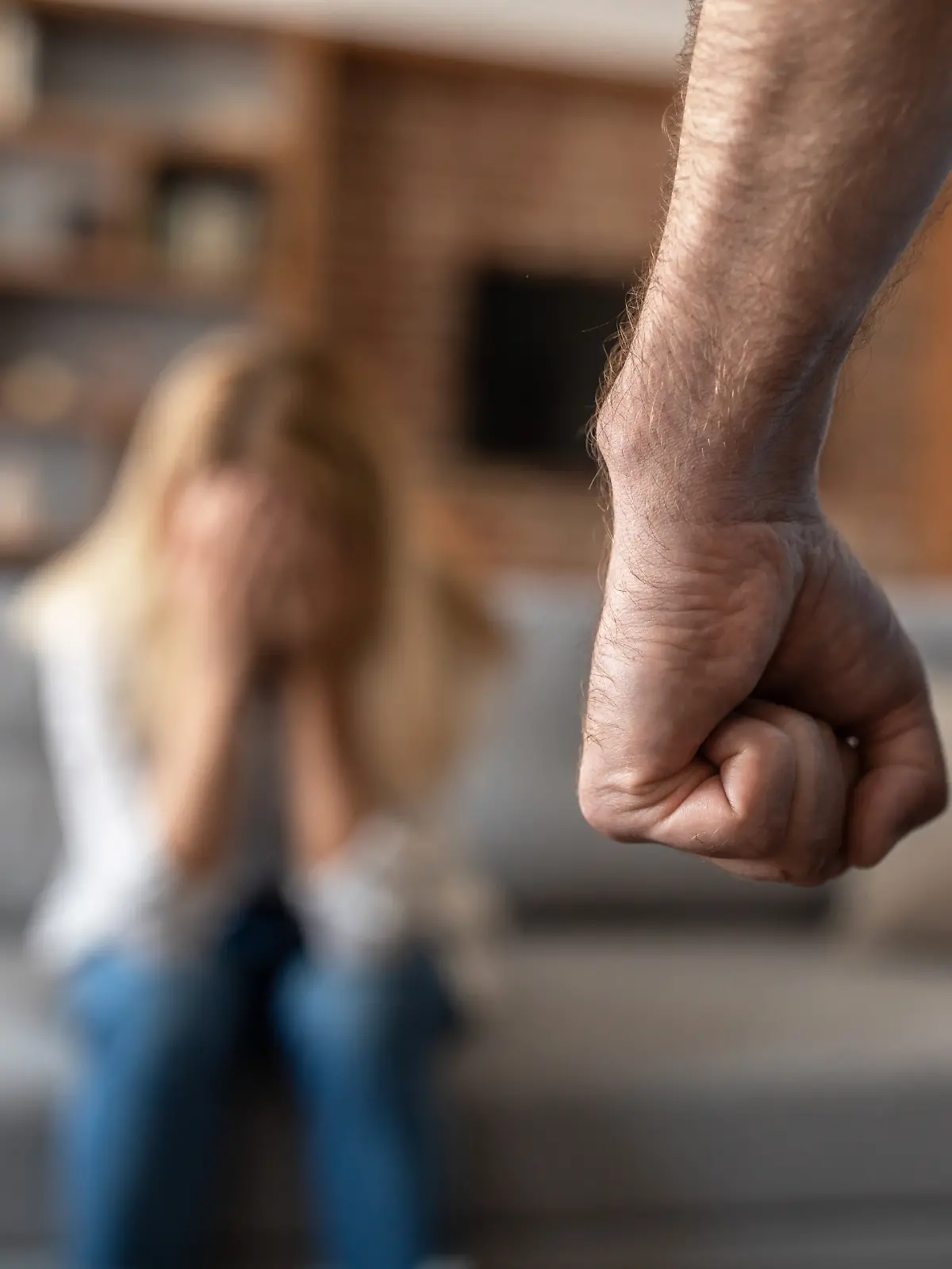 Eine verängstigte, weinende Frau fürchtet ihren Mann, der sie im Wohnzimmer mit der Faust bedroht (Nahaufnahme). Beziehungsprobleme, Missbrauch, Schläge  und häusliche Gewalt