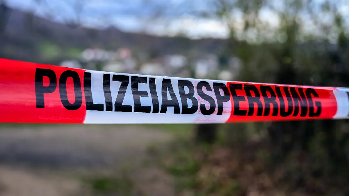 German  crime  scene  or  police  barrier  tape  in  a  park  saying  'Polizeiabsperrung',  meaning