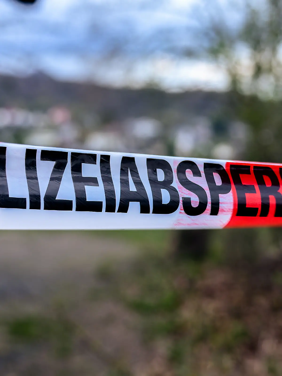 German  crime  scene  or  police  barrier  tape  in  a  park  saying  'Polizeiabsperrung',  meaning