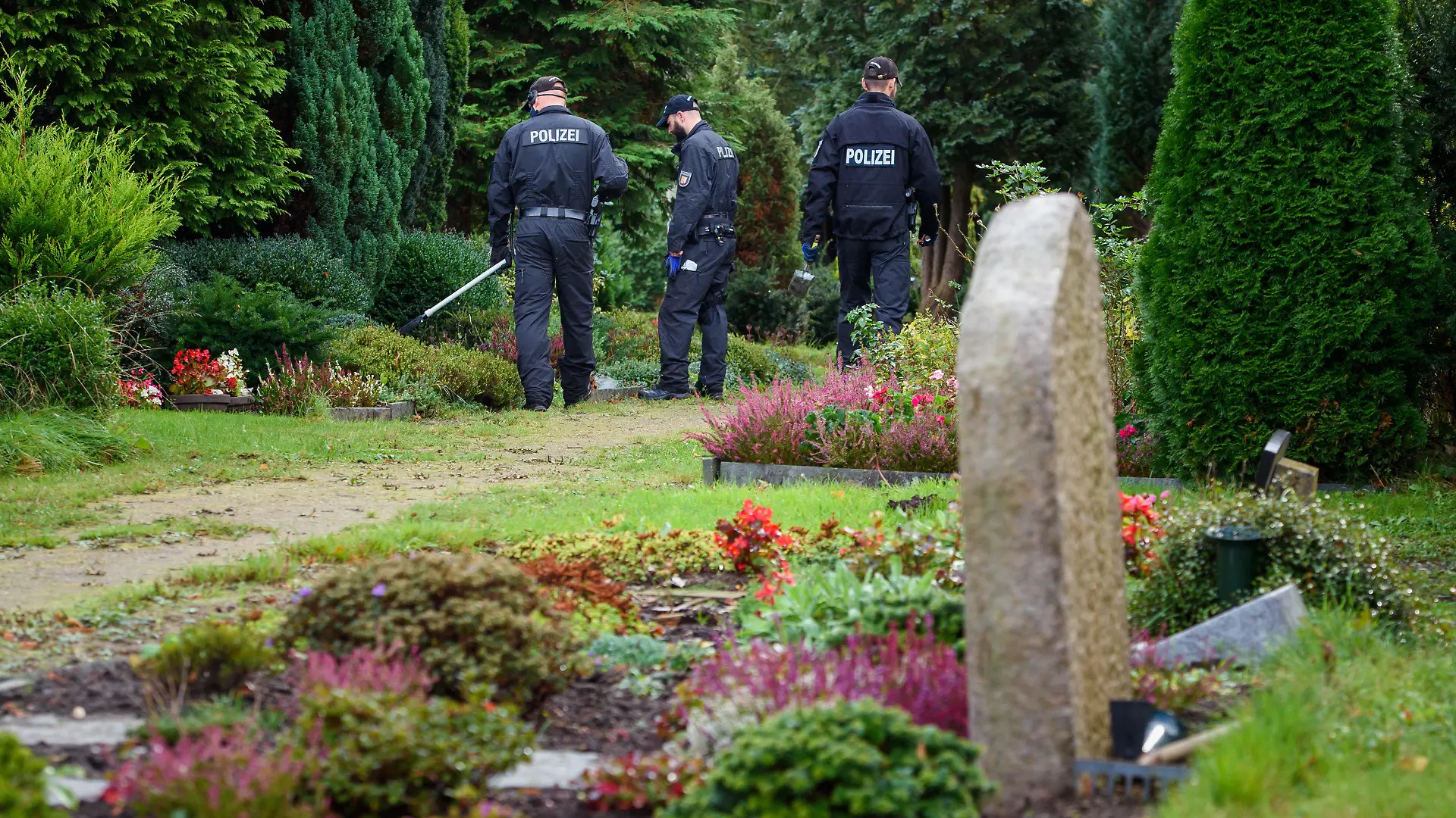 07.10.2020, Schleswig-Holstein, Rendsburg: Polizisten gehen mit einem Metalldetektor über den Rendsburger Friedhof. Die Beamten suchen nach möglichen Beweismitteln im Fall einer Ende September in einer Mietwohnung gegenüber dem Friedhof getöteten Frau. Foto: Gregor Fischer/dpa +++ dpa-Bildfunk +++