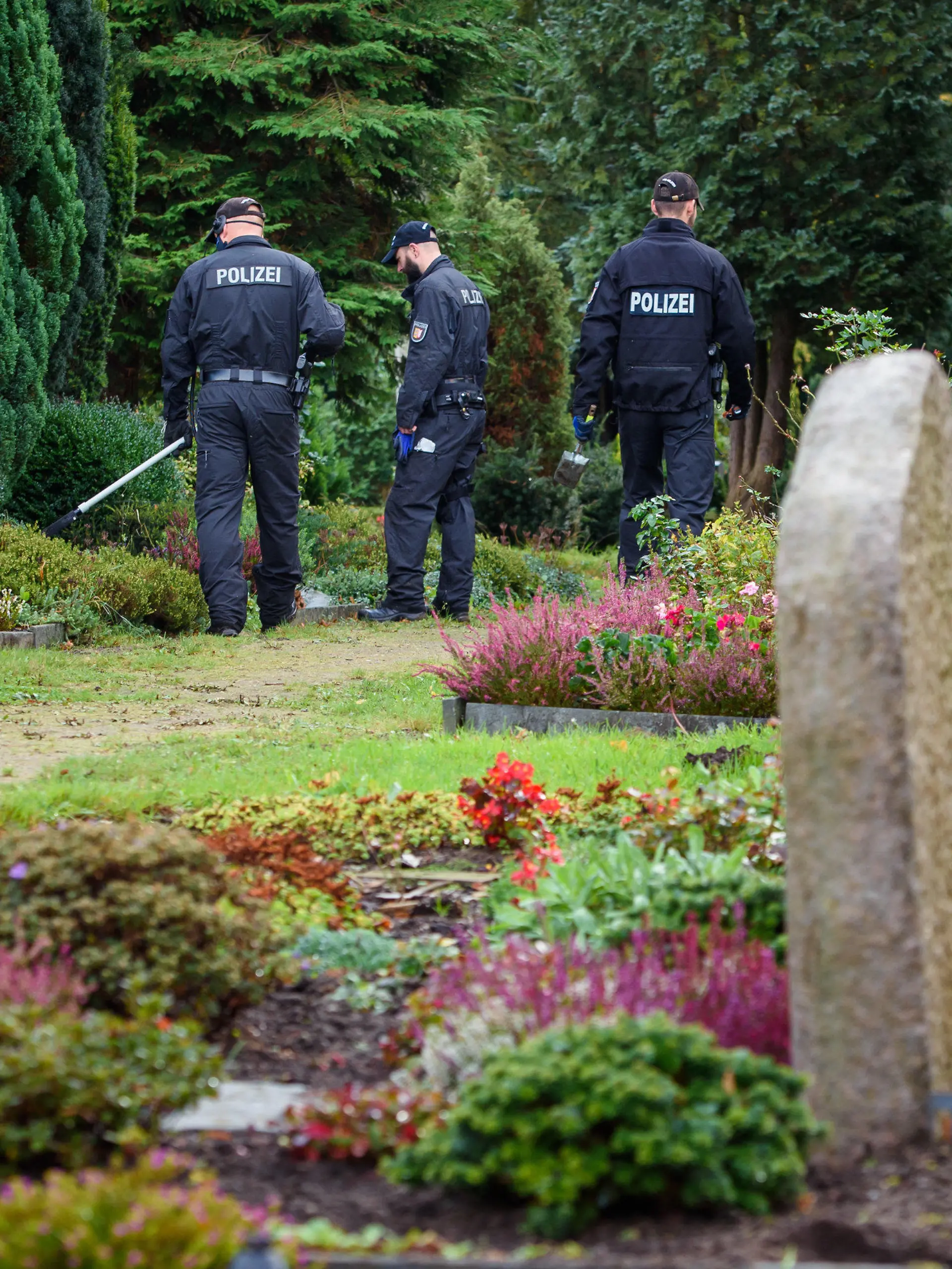 07.10.2020, Schleswig-Holstein, Rendsburg: Polizisten gehen mit einem Metalldetektor über den Rendsburger Friedhof. Die Beamten suchen nach möglichen Beweismitteln im Fall einer Ende September in einer Mietwohnung gegenüber dem Friedhof getöteten Frau. Foto: Gregor Fischer/dpa +++ dpa-Bildfunk +++