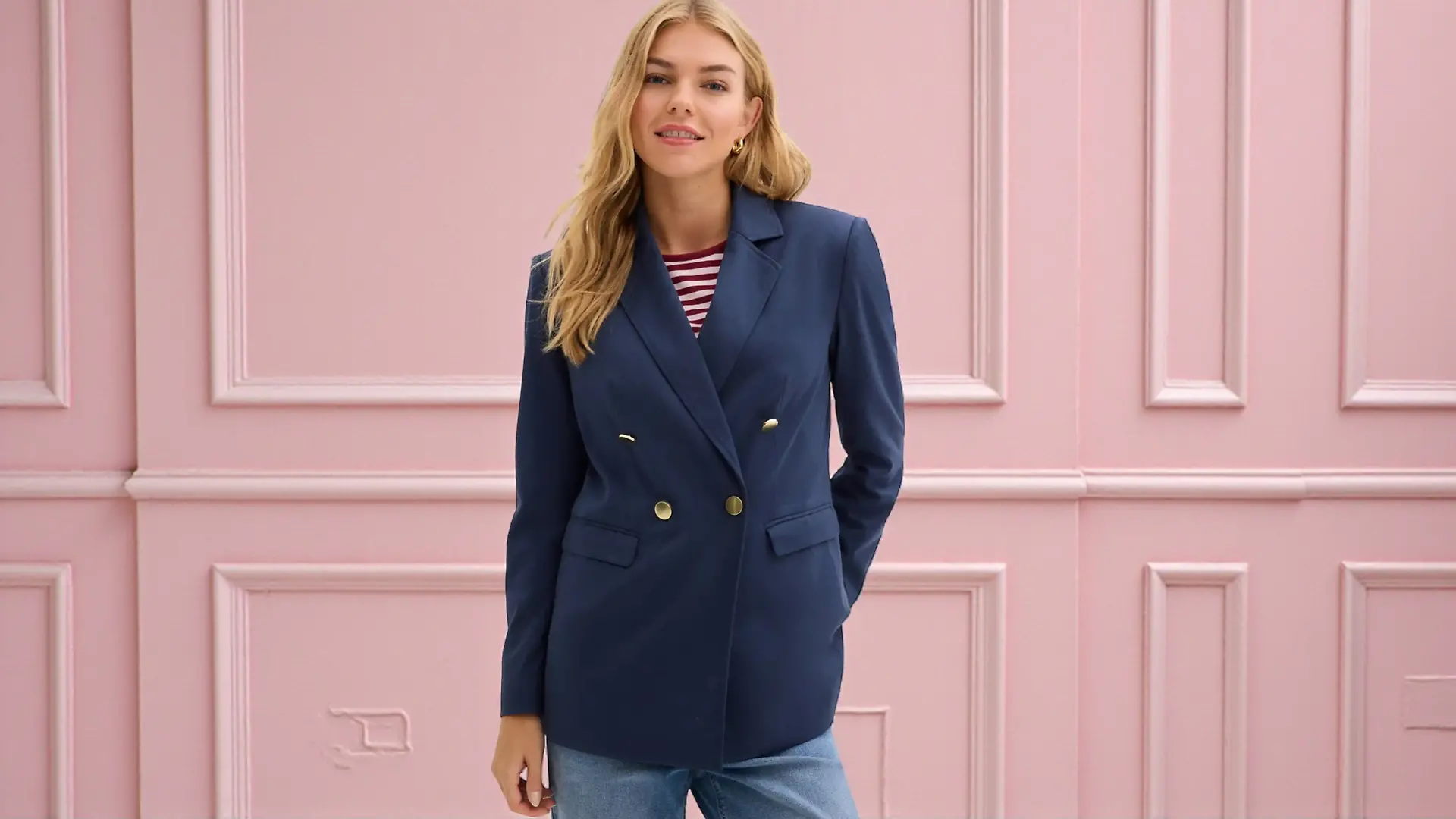 Model in blauem Blazer vor rosa Hintergrund.