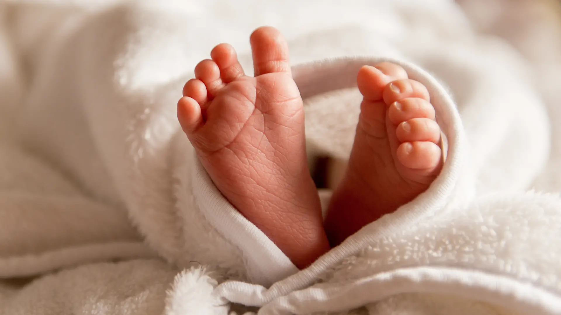 Bare feet of a cute newborn baby in warm white blanket. Small bare feet of a little baby girl or boy. Sleeping newborn child.