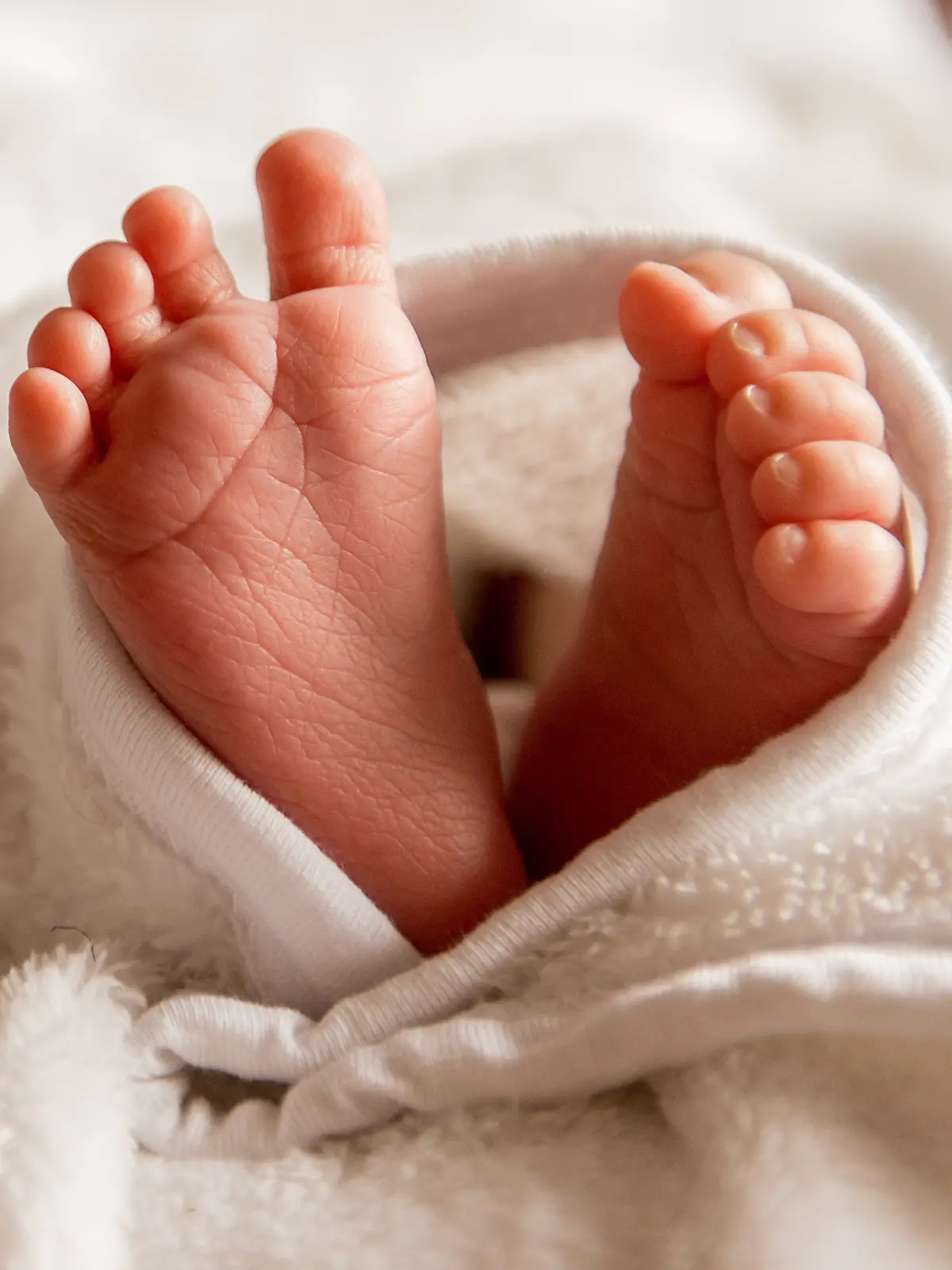 Bare feet of a cute newborn baby in warm white blanket. Small bare feet of a little baby girl or boy. Sleeping newborn child.