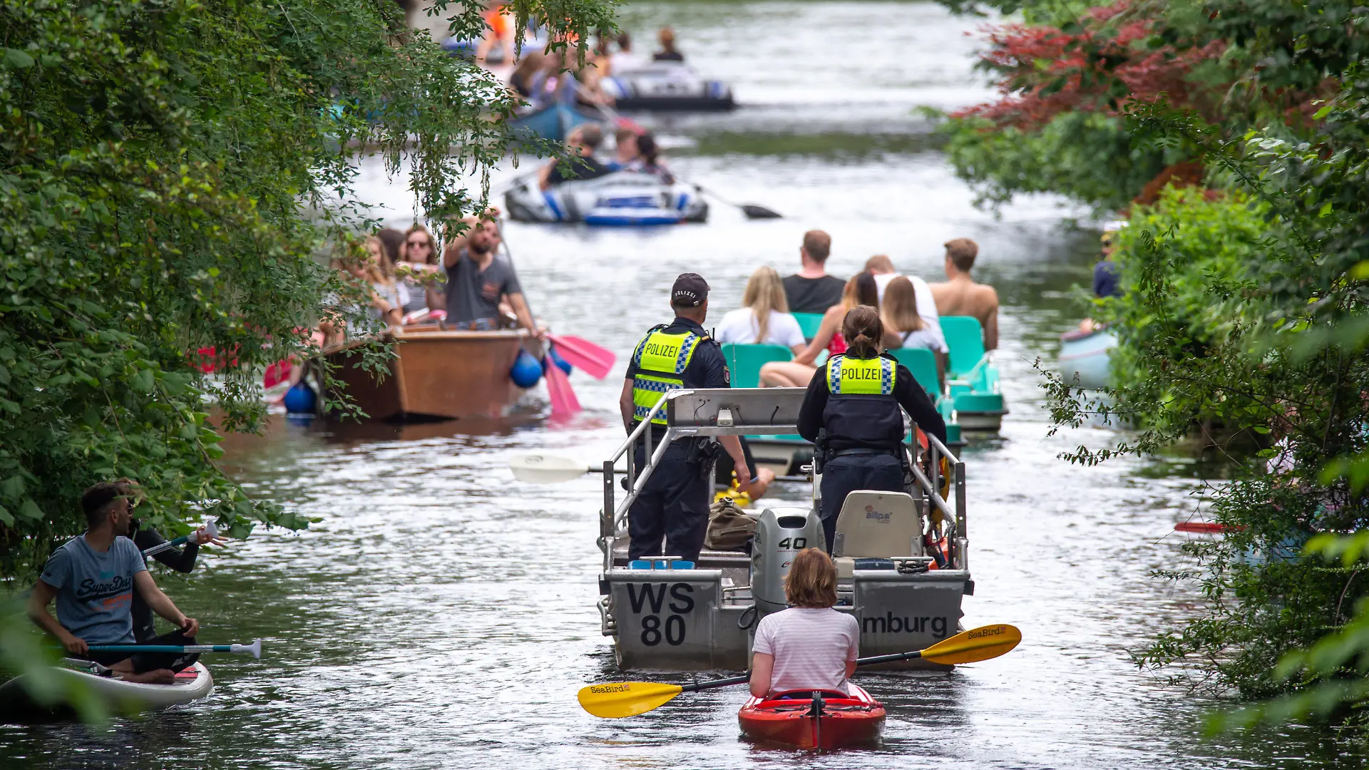 PRODUKTION - 10.07.2021, Hamburg: Wasserschutzpolizisten fahren mit einem Motorboot über den Mühlenkampkanal, auf dem viele mit Freizeitsportler unterwegs sind. An heißen Sommertagen wird es eng auf der Alster - vor allem in den Kanälen. Gefahren für Freizeitkapitäne und Natur sind die Folge. (zu dpa "Enge auf der Hamburger Alster - Suche nach Lösungen schwierig") Foto: Jonas Walzberg/dpa +++ dpa-Bildfunk +++