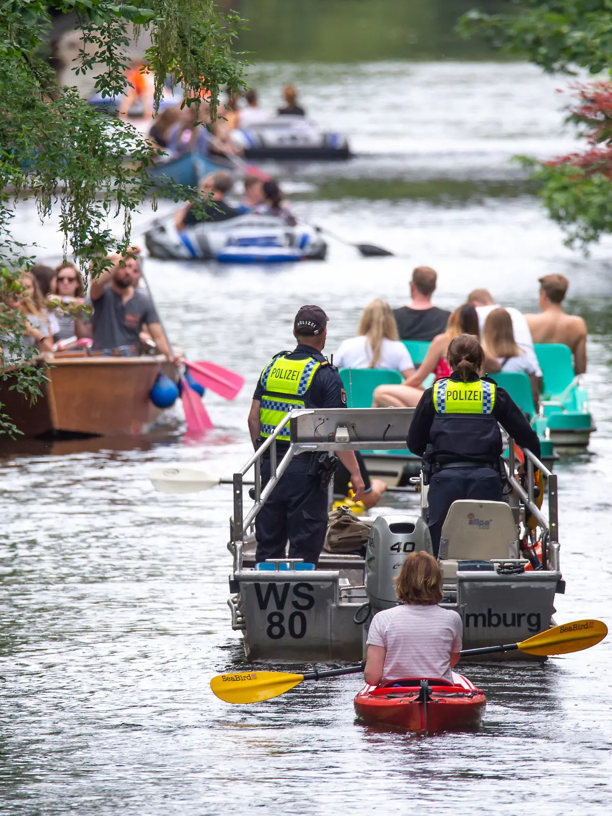 PRODUKTION - 10.07.2021, Hamburg: Wasserschutzpolizisten fahren mit einem Motorboot über den Mühlenkampkanal, auf dem viele mit Freizeitsportler unterwegs sind. An heißen Sommertagen wird es eng auf der Alster - vor allem in den Kanälen. Gefahren für Freizeitkapitäne und Natur sind die Folge. (zu dpa "Enge auf der Hamburger Alster - Suche nach Lösungen schwierig") Foto: Jonas Walzberg/dpa +++ dpa-Bildfunk +++