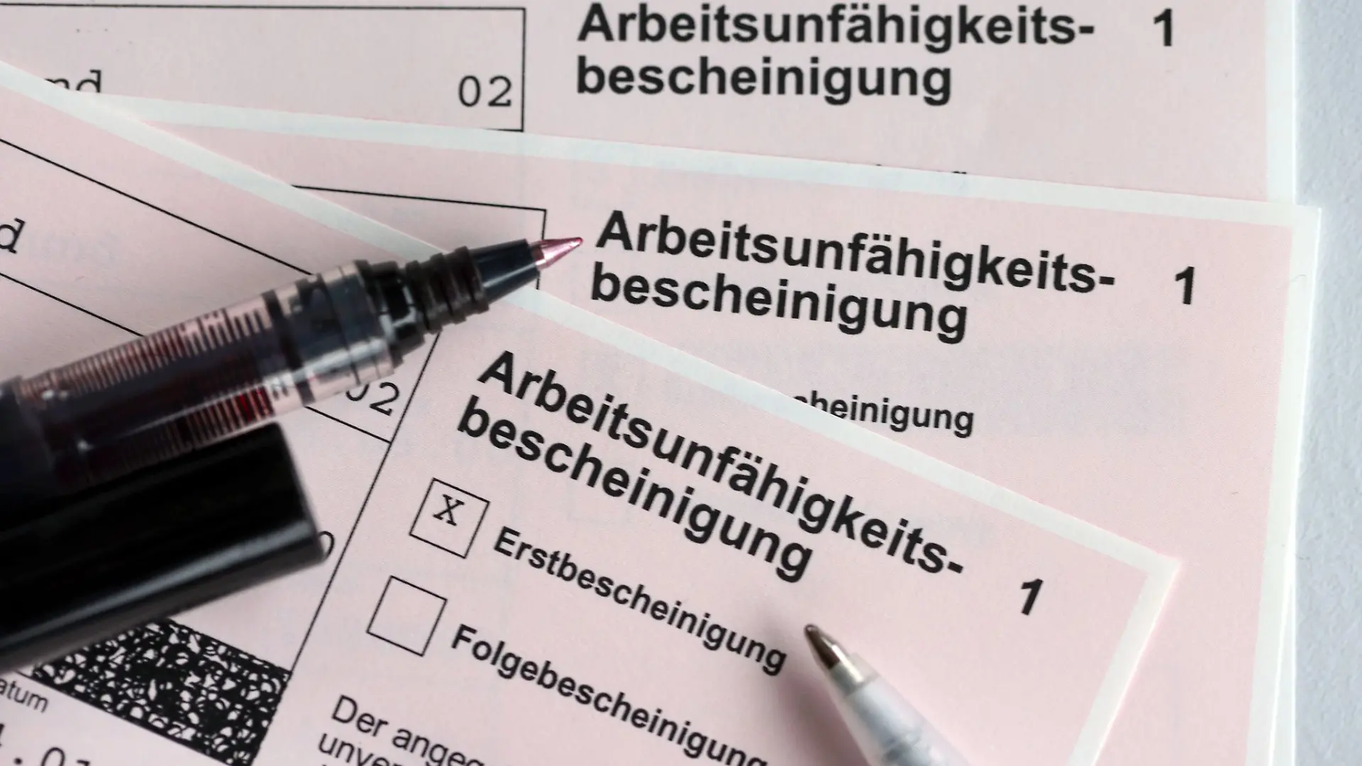 Stifte liegen auf Arbeitsunfähigkeitsbescheinigungen.