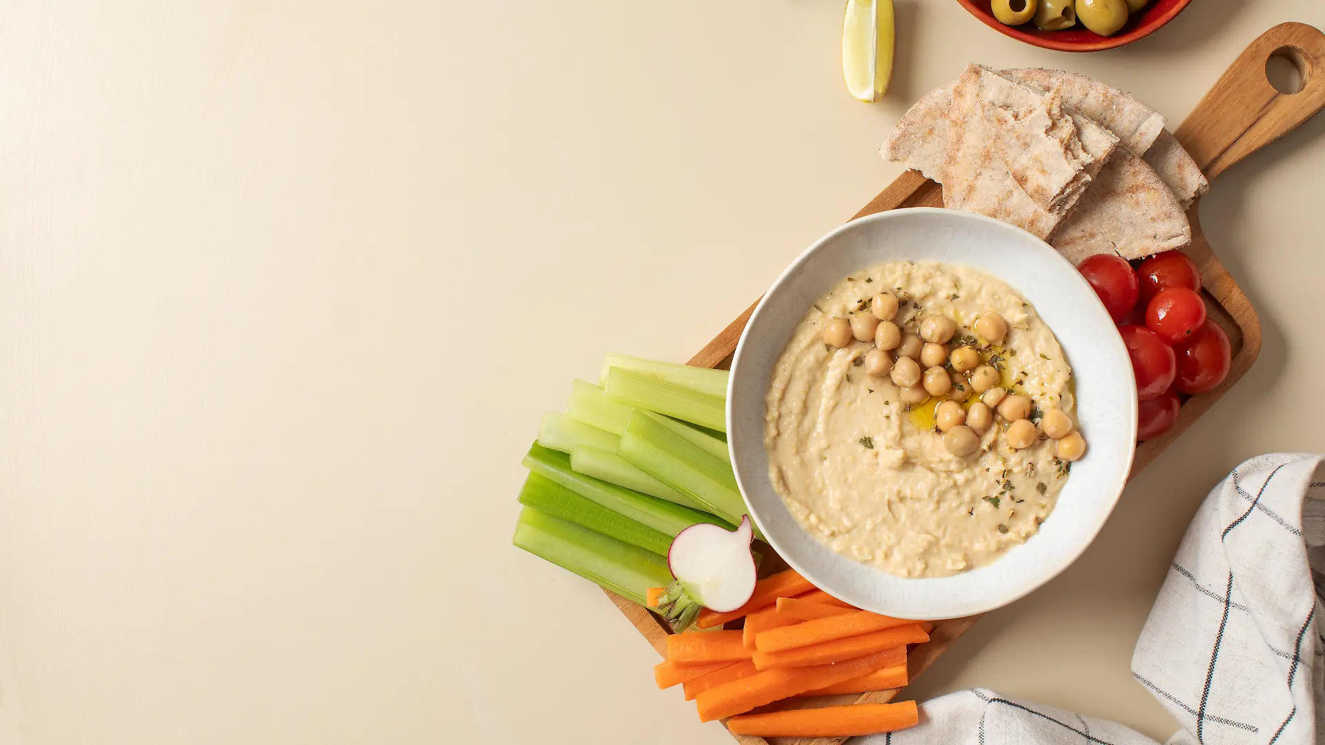 Frischer Hummus in einer Schüssel auf einem Holzbrett mit Pita, Sellerie und Karotten. 