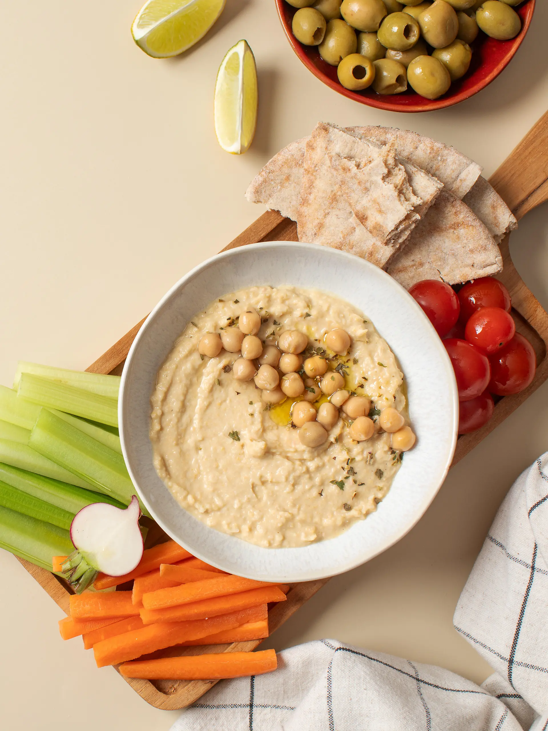 Frischer Hummus in einer Schüssel auf einem Holzbrett mit Pita, Sellerie und Karotten.