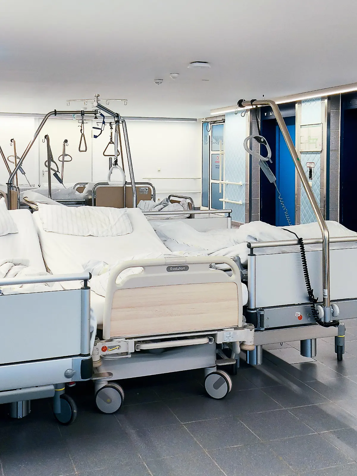 Mehrere gebrauchte Krankenhausbetten stehen unbesetzt auf einem Flur einer Klinik. Die Betten wurden bereits genutzt und sind aktuell nicht belegt. Der Klinikalltag mit leerstehenden Betten im Spannungsfeld von Entlassungen, Personalengpässen und strukturellen Herausforderungen im Gesundheitswesen