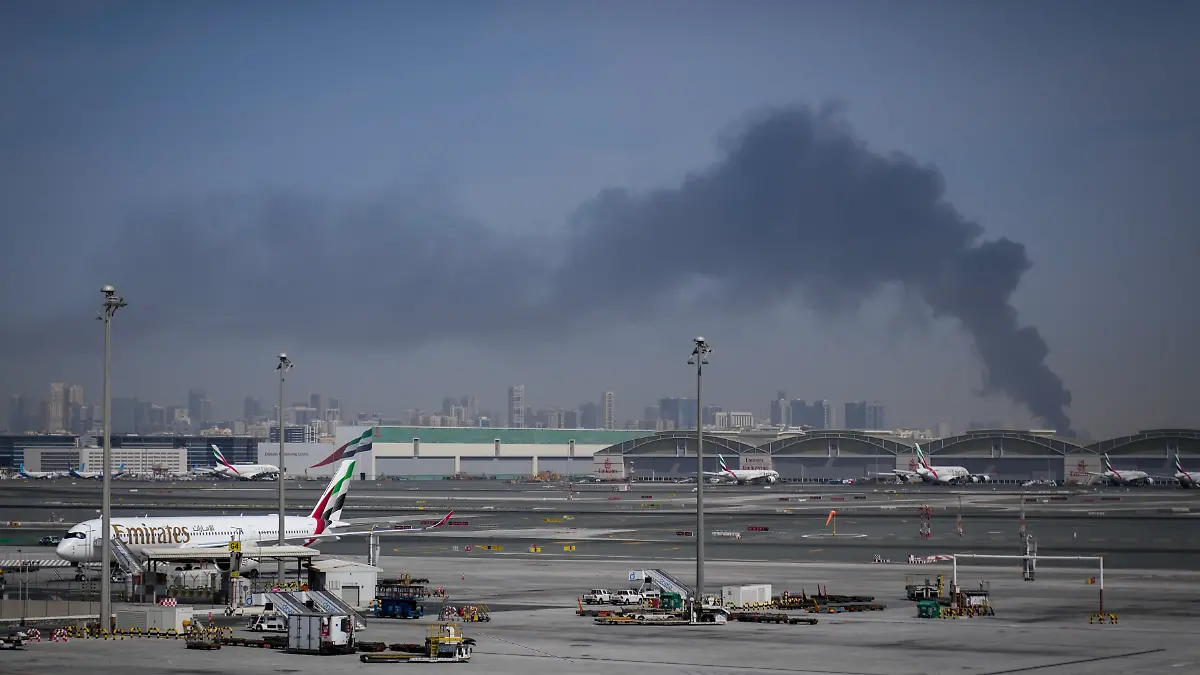 Eine Rauchwolke, verursacht durch einen iranischen Angriff, ist im Hintergrund zu sehen, während Flugzeuge der Emirates nach der Schließung des Flughafens auf dem Dubai International Airport geparkt sind. +++ dpa-Bildfunk +++