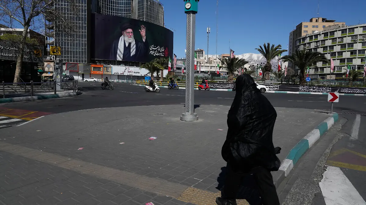 Eine Frau überquert einen fast menschenleeren Platz mit einer Plakatwand im Hintergrund, die ein Porträt des getöteten iranischen Obersten Führers Chamenei zeigt. +++ dpa-Bildfunk +++