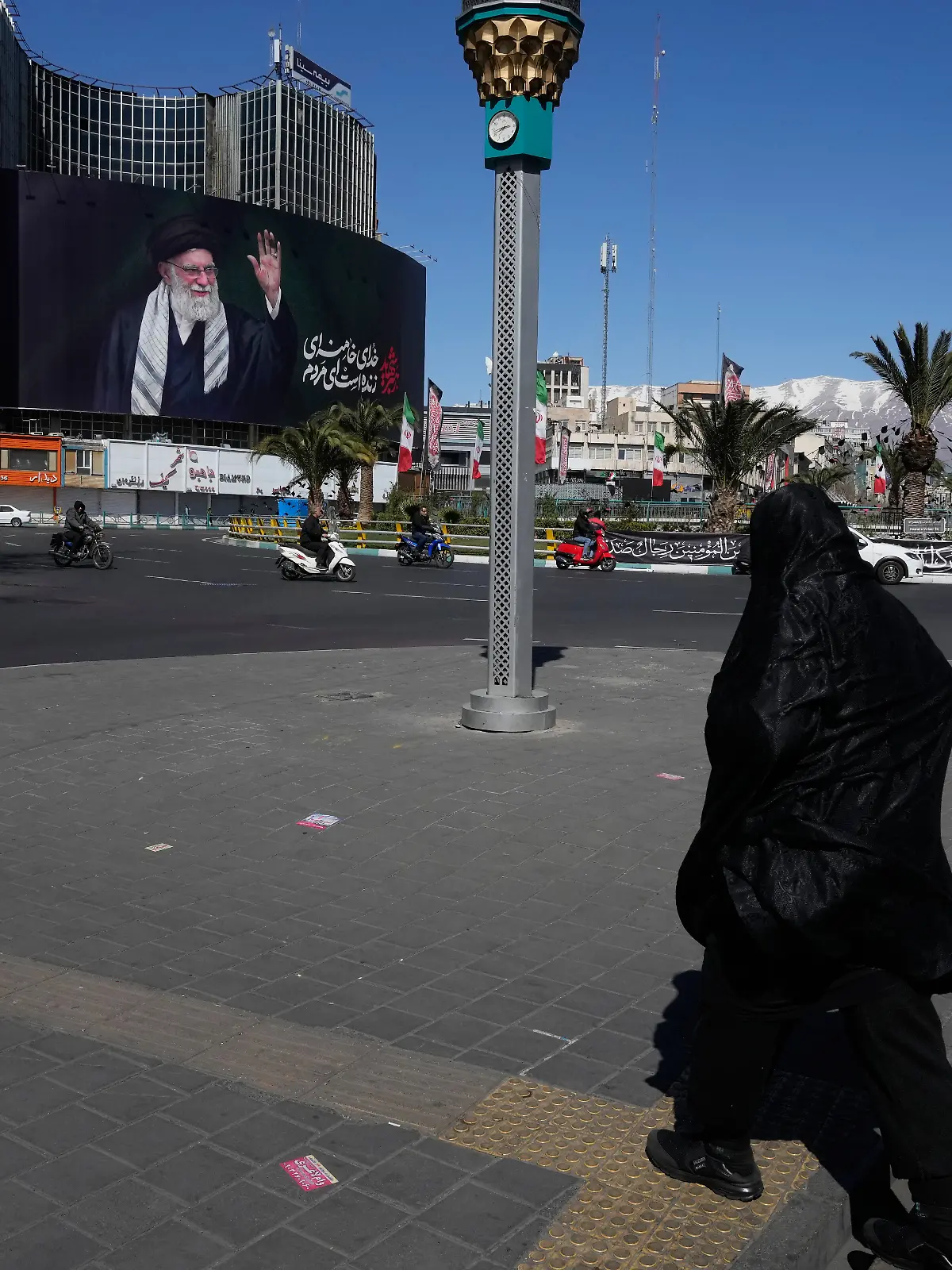 Eine Frau überquert einen fast menschenleeren Platz mit einer Plakatwand im Hintergrund, die ein Porträt des getöteten iranischen Obersten Führers Chamenei zeigt. +++ dpa-Bildfunk +++