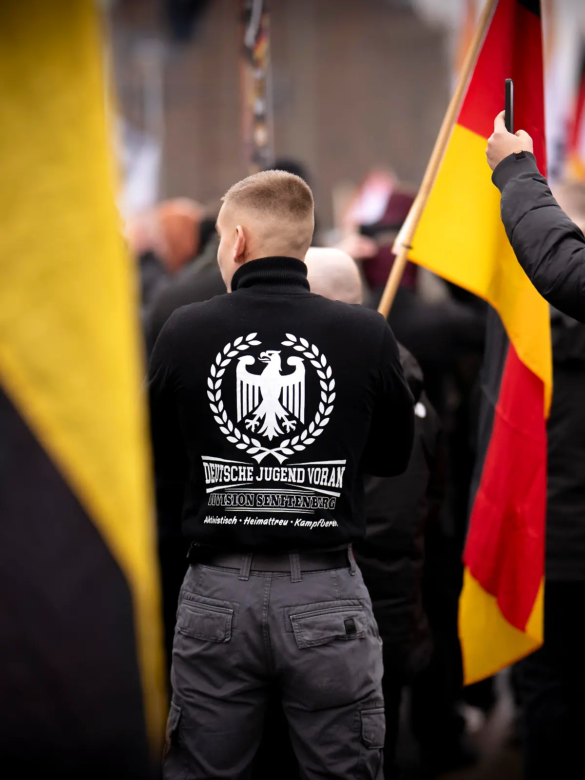 DEU, Deutschland, Germany, Berlin, 29.11.2025 Demonstrant mit Shirt Symbol Adler und Logo Deutsche Jugend Voran Division Senftenberg Aktivistisch Heimattreu Kampfbereit bei dem Marsch Kundgebung und Demonstration der rechtsextremen Partei Die Heimat ehemals NPD unter dem Motto Betrueger und Kriminelle Auslaender raus und Heimatschützer in Berlin Deutschland . Neben Mitgliedern der Heimat und der Jugendorganisation Junge Nationalisten JN fanden sich auch Mitglieder Deutsche Jugend Voran DJV und der sog. Jaegergruppe Jägergruppe . Ein breites Buendnis von der antifaschistischen Aktion antifa bis zu Omas gegen rechts konnte mit einer Blockade die eigentliche Demo verhindern en: Demonstrator wearing a shirt with the eagle symbol and the Logo German Youth Forward Division Senftenberg activist patriotic ready for battle at the march and demonstration of the far-right party Die Heimat formerly NPD under the motto Cheaters and Criminals, Foreigners Out, and Homeland Protectors in Berlin Germany . Besides members of the Heimat youth organization Young Nationalists Junge Nationalisten JN , members of the Deutsche Jugend Voran German Youth Forward DJV and the so-called Hunter Group Jägergruppe were also present. A broad alliance, ranging from the anti-fascist action group Antifa to Grandmas Against the Right successfully blocked the demonstration