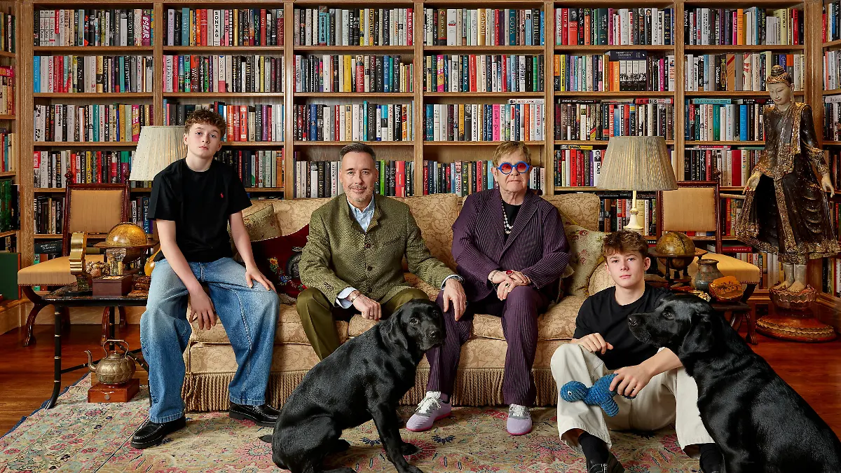 Das Bild zeigt die vierköpfige Familie beisammen auf einem Sofa inmitten von Bücherregalen.