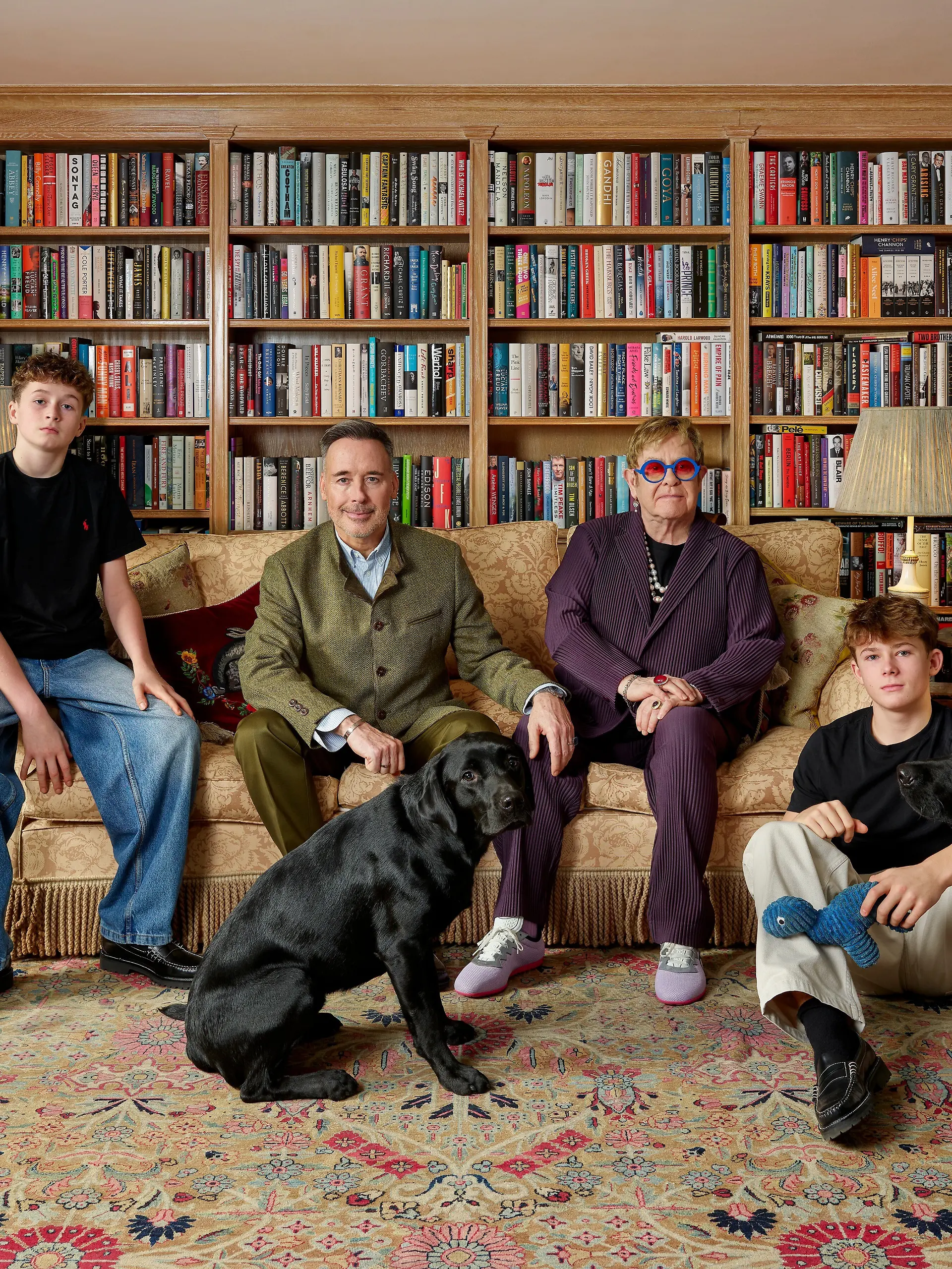 Das Bild zeigt die vierköpfige Familie beisammen auf einem Sofa inmitten von Bücherregalen. 