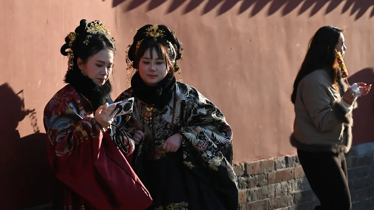 PRODUKTION - 17.02.2026, China, Peking: Zwei Frauen fotografieren sich an der roten Mauer des bei Peking-Touristen beliebten Trommelturms. Auf sozialen Medien macht ein Trend die Runde, sich besonders chinesisch zu verhalten und Gebräuche nachzuahmen. (zu dpa: «Warme Füße und Reisbrei: Warum China plötzlich Trend ist») Foto: Johannes Neudecker/dpa +++ dpa-Bildfunk +++
