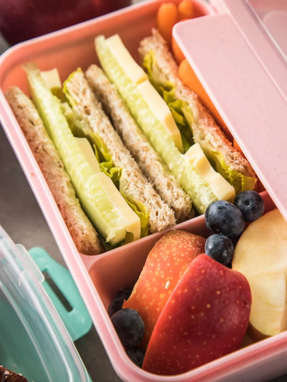 ILLUSTRATION - Eine Brotdose mit Vollkorn-Toast (belegt mit Gurkenstreifen, Maasdammer Kaese und Salat), dazu Blaubeeren und Apfelschnitze ist am 25.08.2023 in Wittenberge zu sehen (gestellte Szene). Foto: Christin Klose