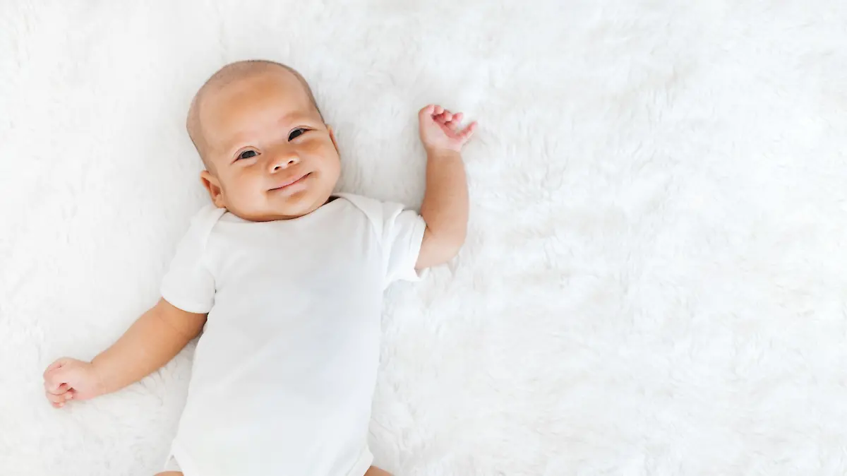 Baby liegt im Bett und lächelt.