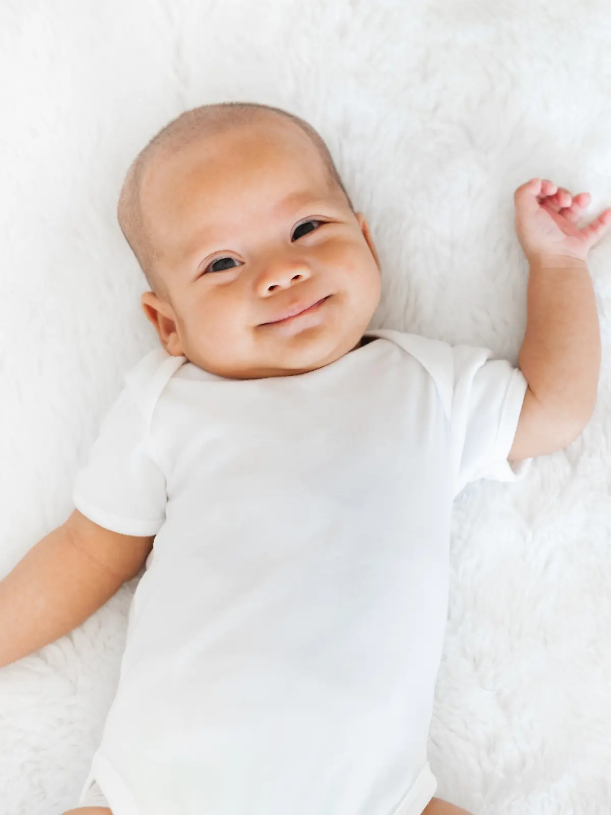 Baby liegt im Bett und lächelt.