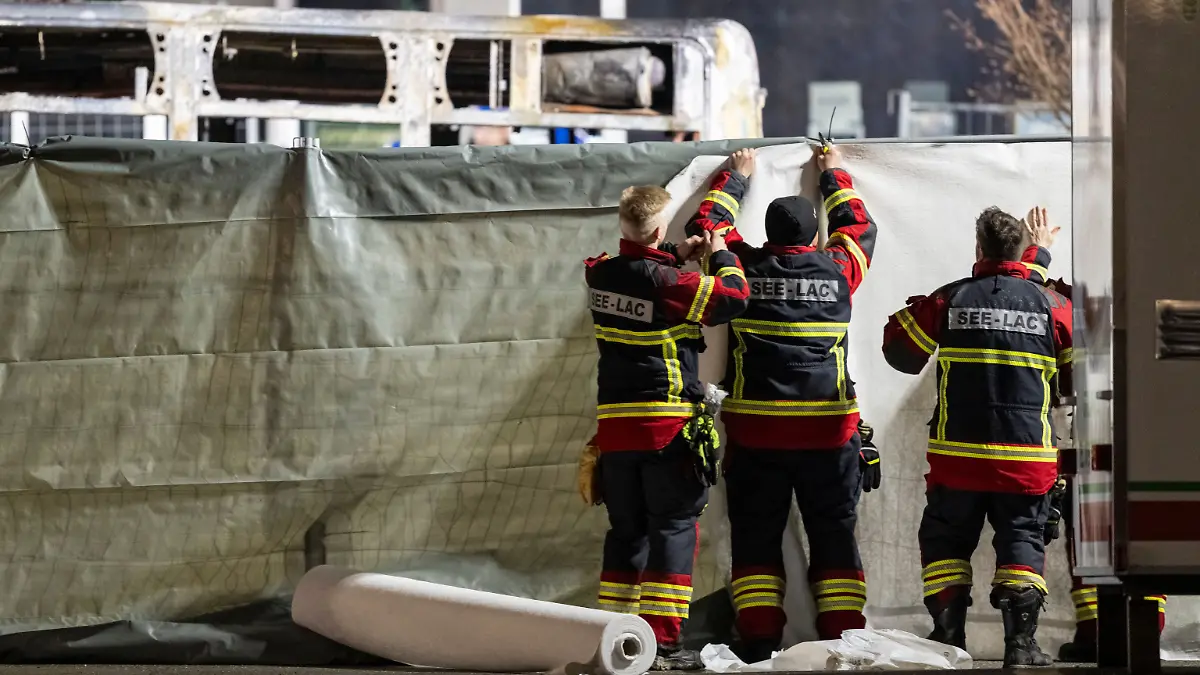 Feuerwehrleute verdecken den Bereich vor der verkohlten Hülle eines ausgebrannten Linienbusses. Bei einem schweren Brand in einem Linienbus sind in der Schweiz sechs Menschen ums Leben gekommen.