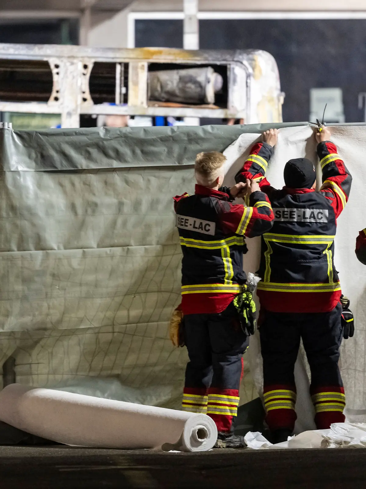 Feuerwehrleute verdecken den Bereich vor der verkohlten Hülle eines ausgebrannten Linienbusses. Bei einem schweren Brand in einem Linienbus sind in der Schweiz sechs Menschen ums Leben gekommen.