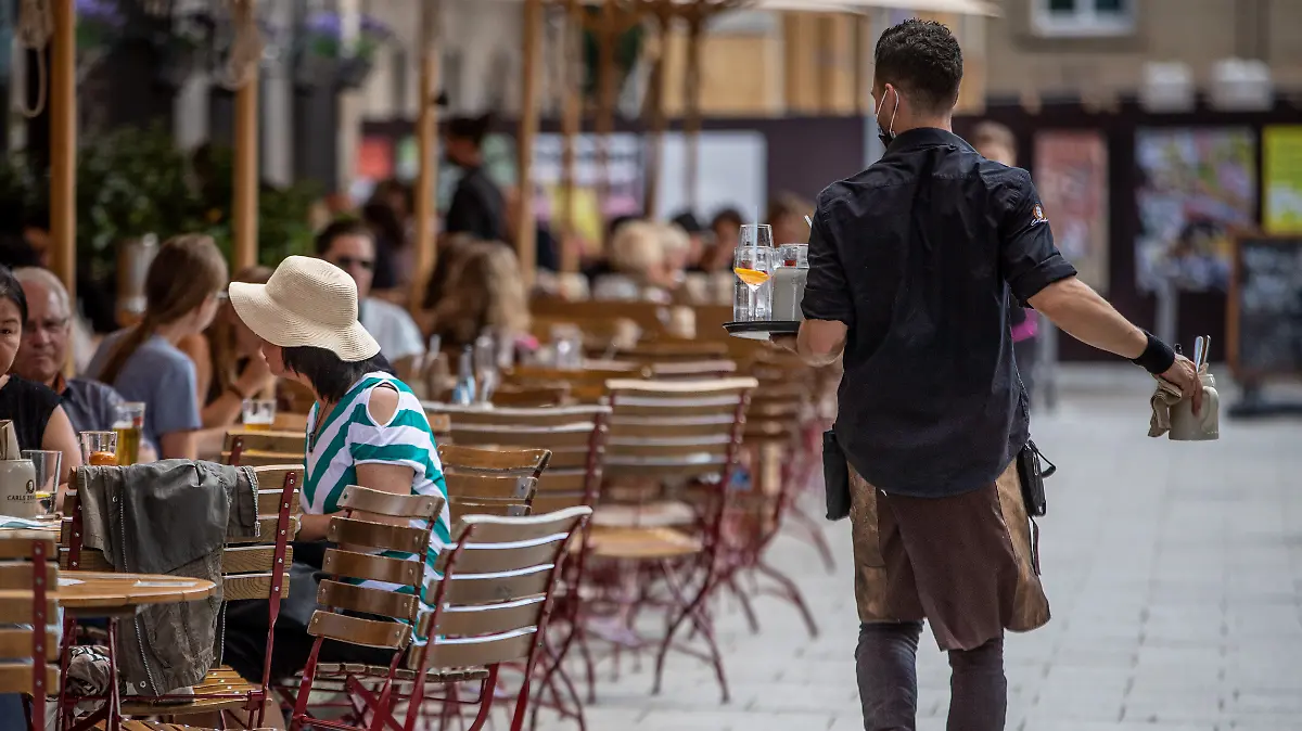 Eine Servicekraft läuft im Außenbereich eines Restaurants an Gästen vorbei. Experten im Gastgewerbe und der Landwirtschaft sehen die Ausstattung mit Saisonkräften in Sachsen-Anhalt in den jeweiligen Branchen verbessert. (zu dpa: «Verbände sehen Situation mit Saisonkräften verbessert») +++ dpa-Bildfunk +++