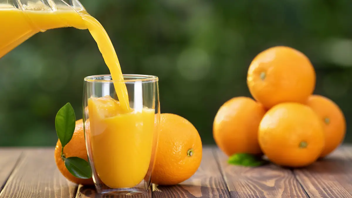 Orangensaft wird in ein Glas gegossen, im Hintergrund Orangen