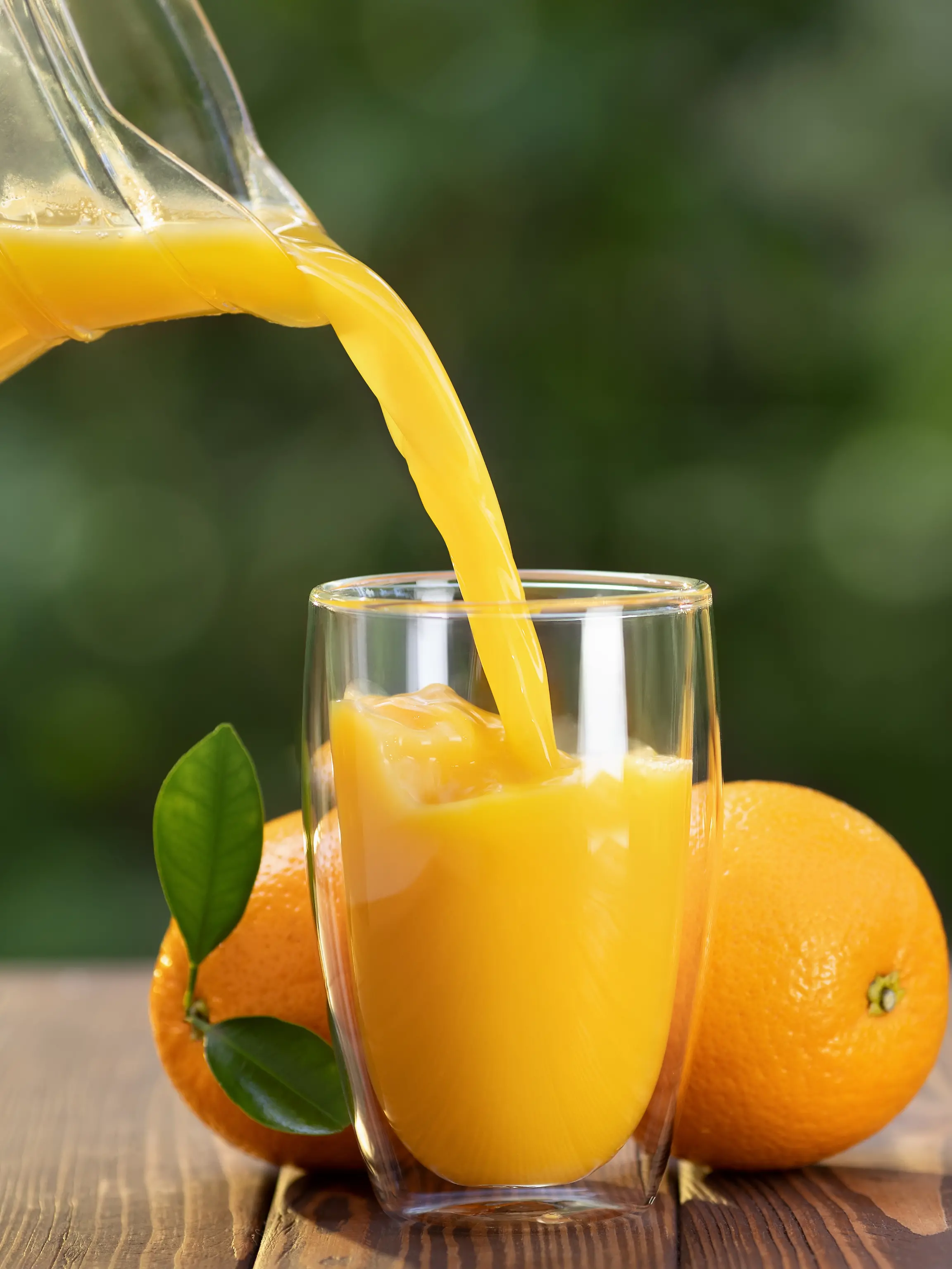 Orangensaft wird in ein Glas gegossen, im Hintergrund Orangen