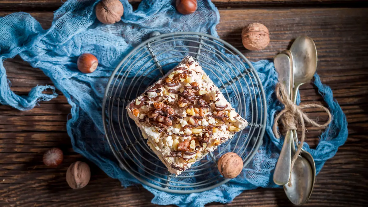 Selbstgemachter Walnuss-Kuchen mit Puddingcreme und Zartbitter-Schokolade auf einem runden Gitter, umgeben von Walnüssen und zwei Löffeln