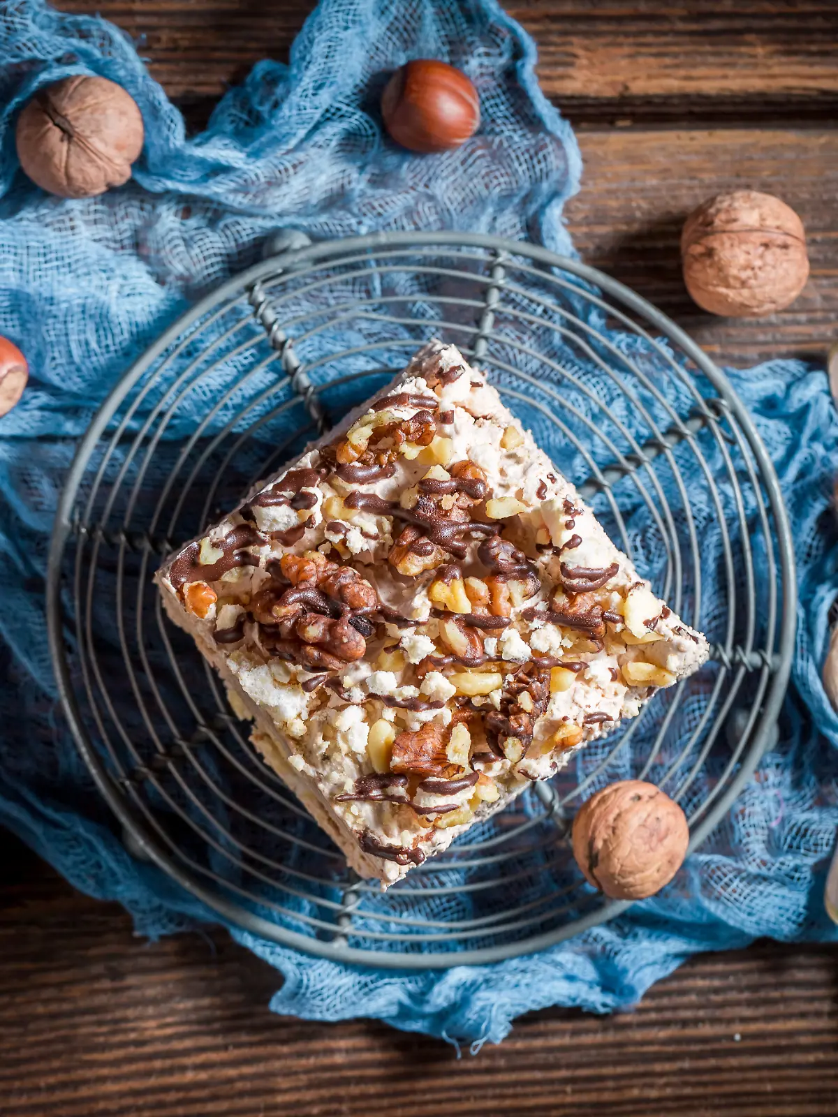 Selbstgemachter Walnuss-Kuchen mit Puddingcreme und Zartbitter-Schokolade auf einem runden Gitter, umgeben von Walnüssen und zwei Löffeln