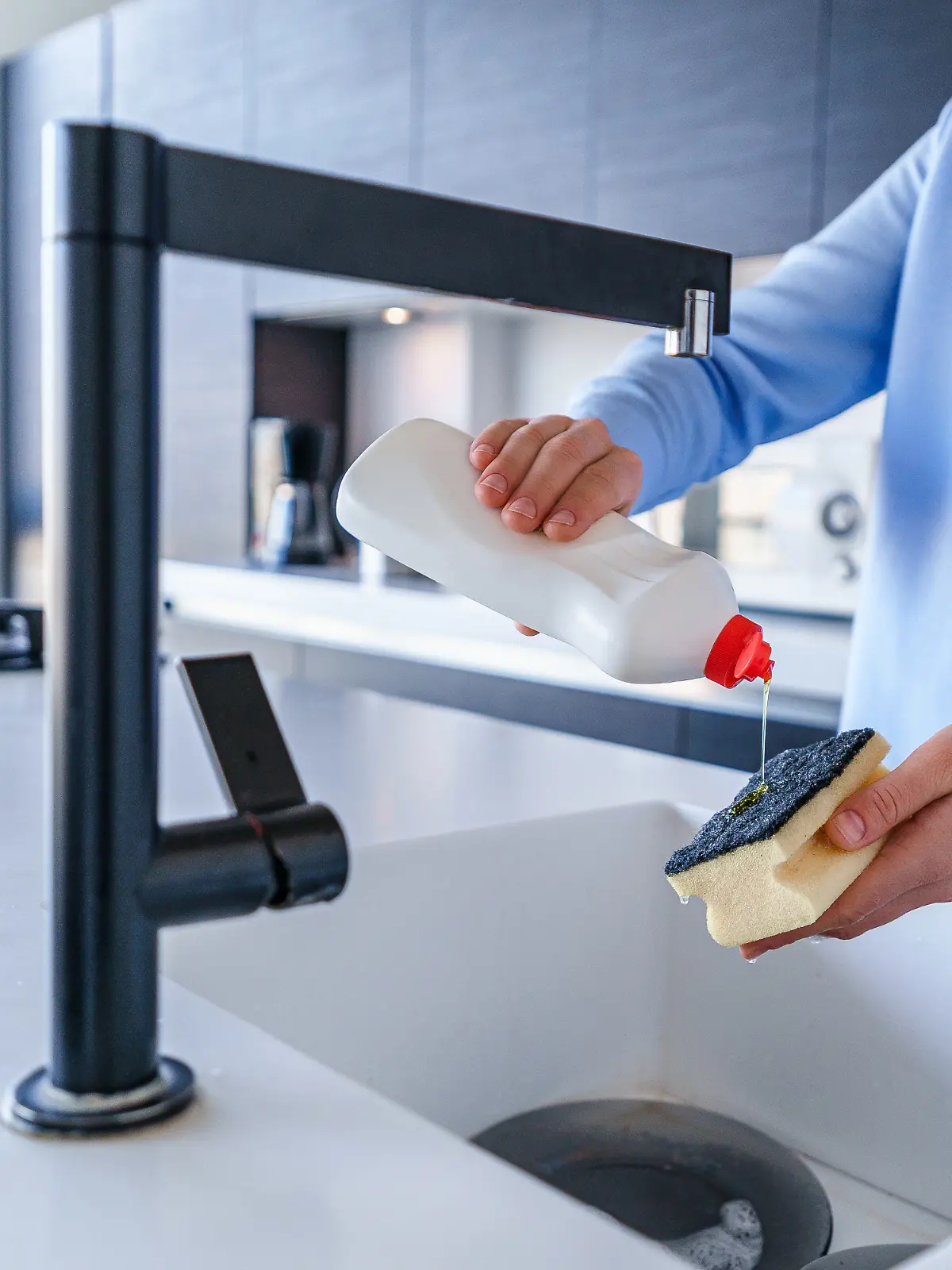 Frau wäscht Geschirr mit Schwamm und Spülmittel ab