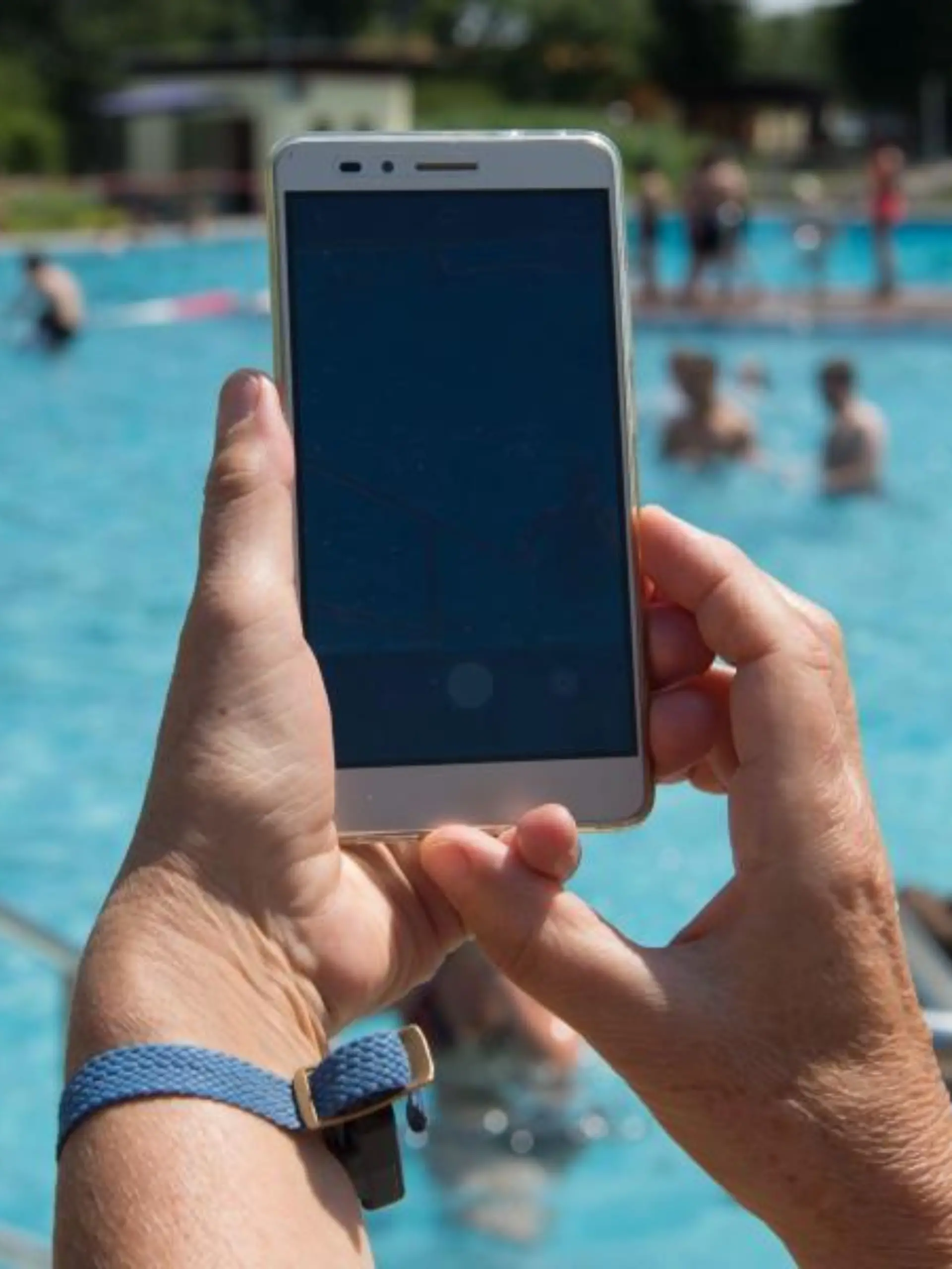 Eine Frau hält im Freibad ein Smartphone in Richtung des Pools